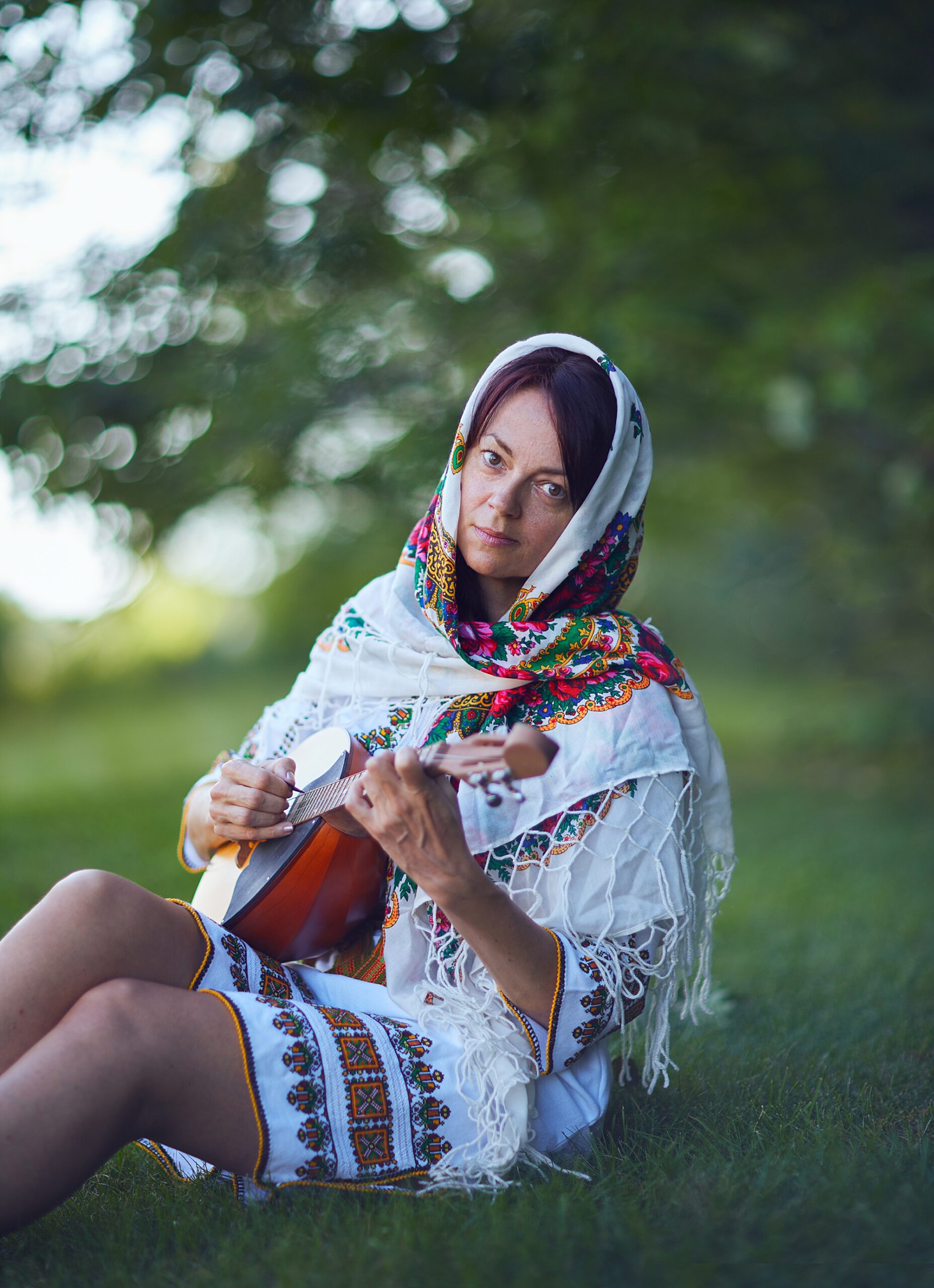 Ukrainian woman playing guitar while sitting on grass