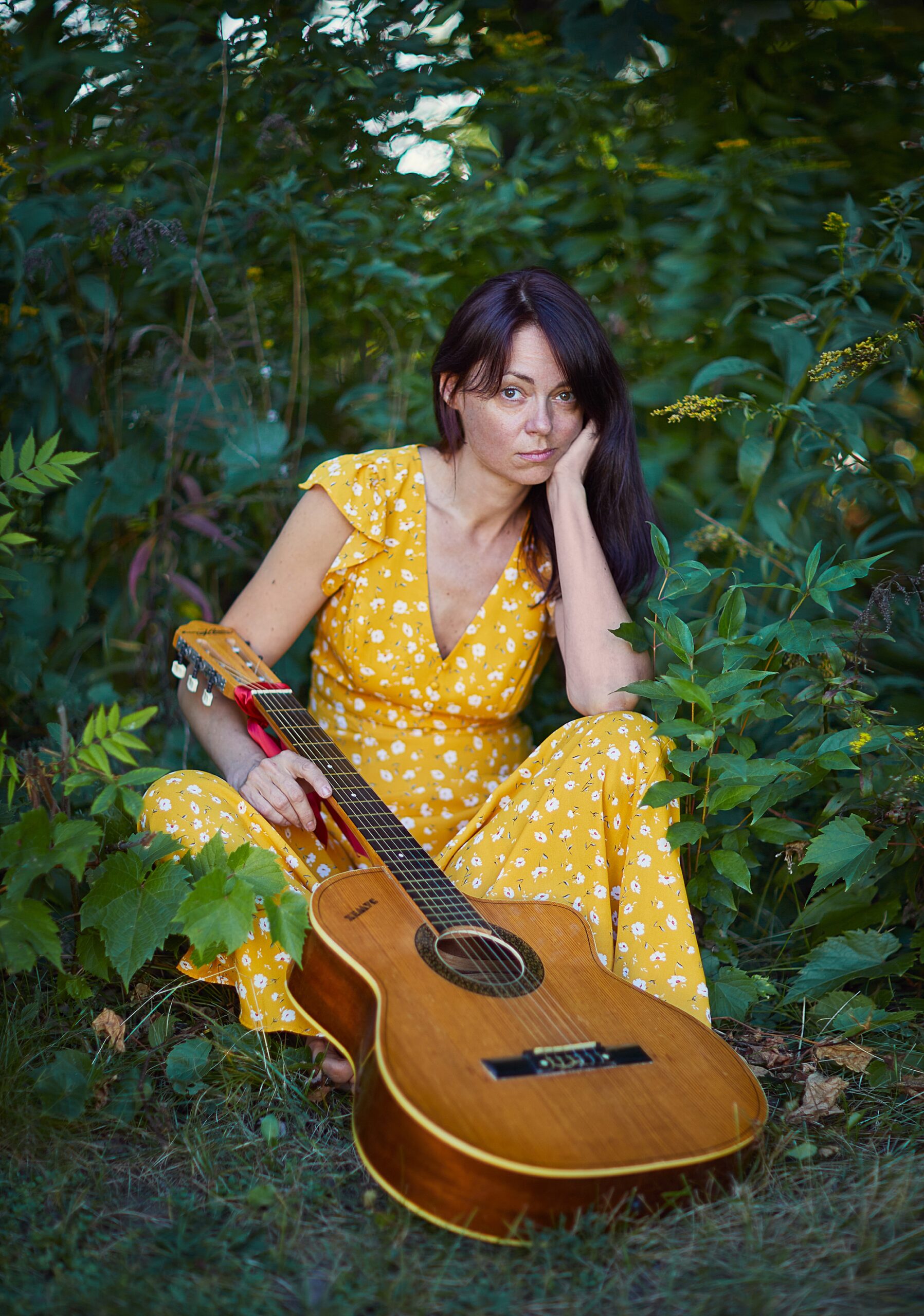 woman holding guitar while sitting in a field