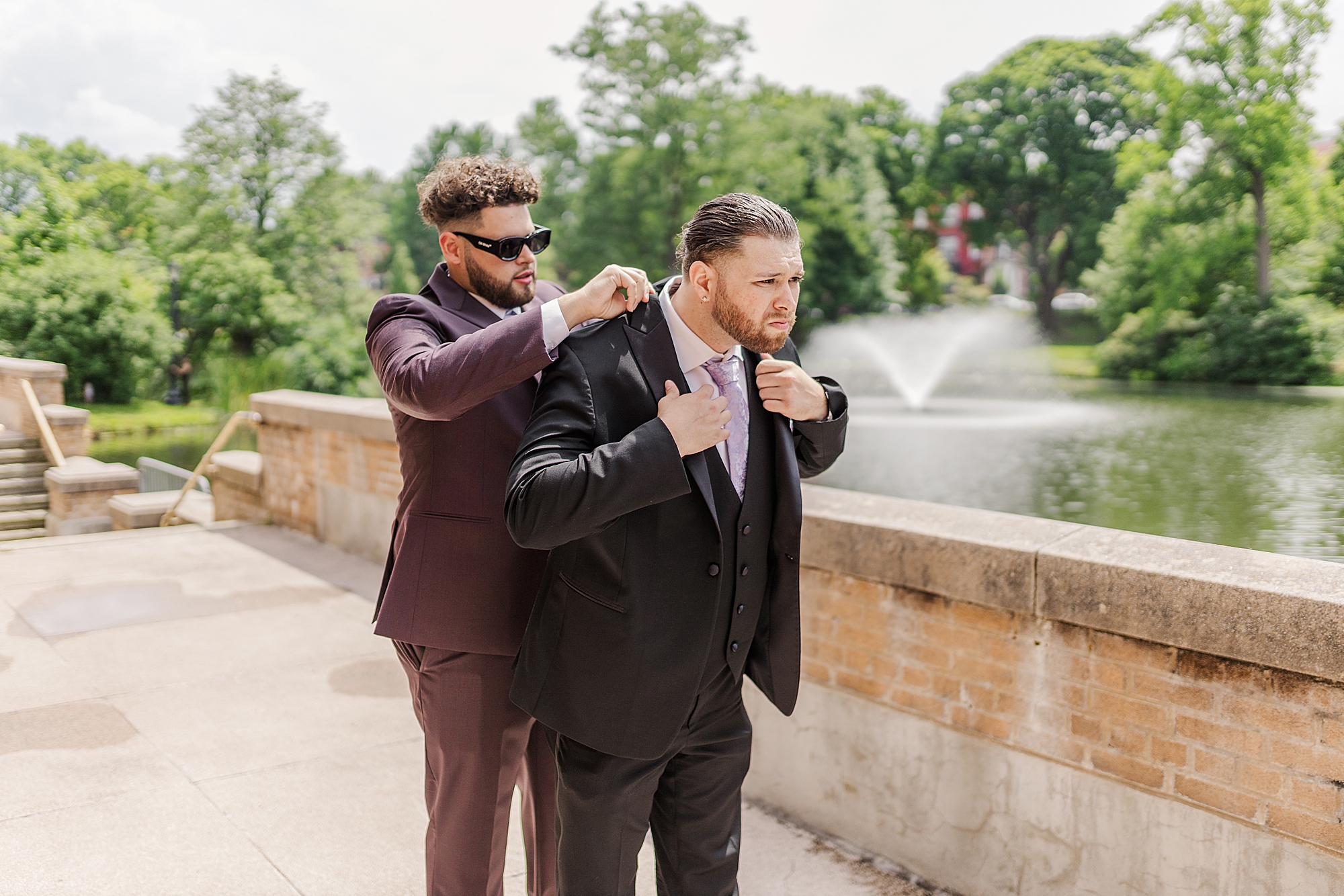 the best man helping groom put his jacket on while outside near body of water 