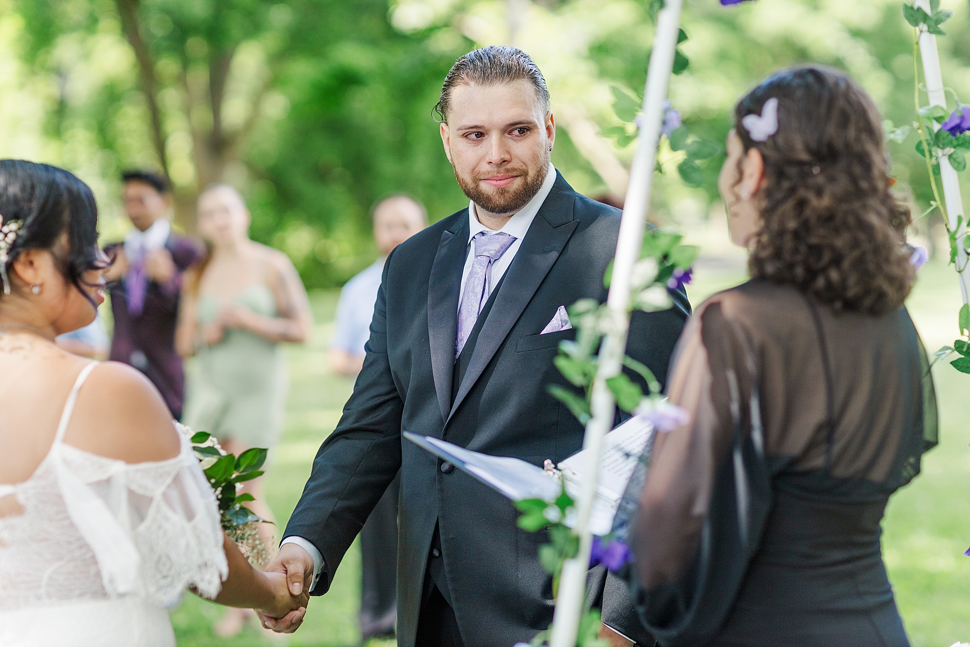 groom holding brides hand while looking at officiant  