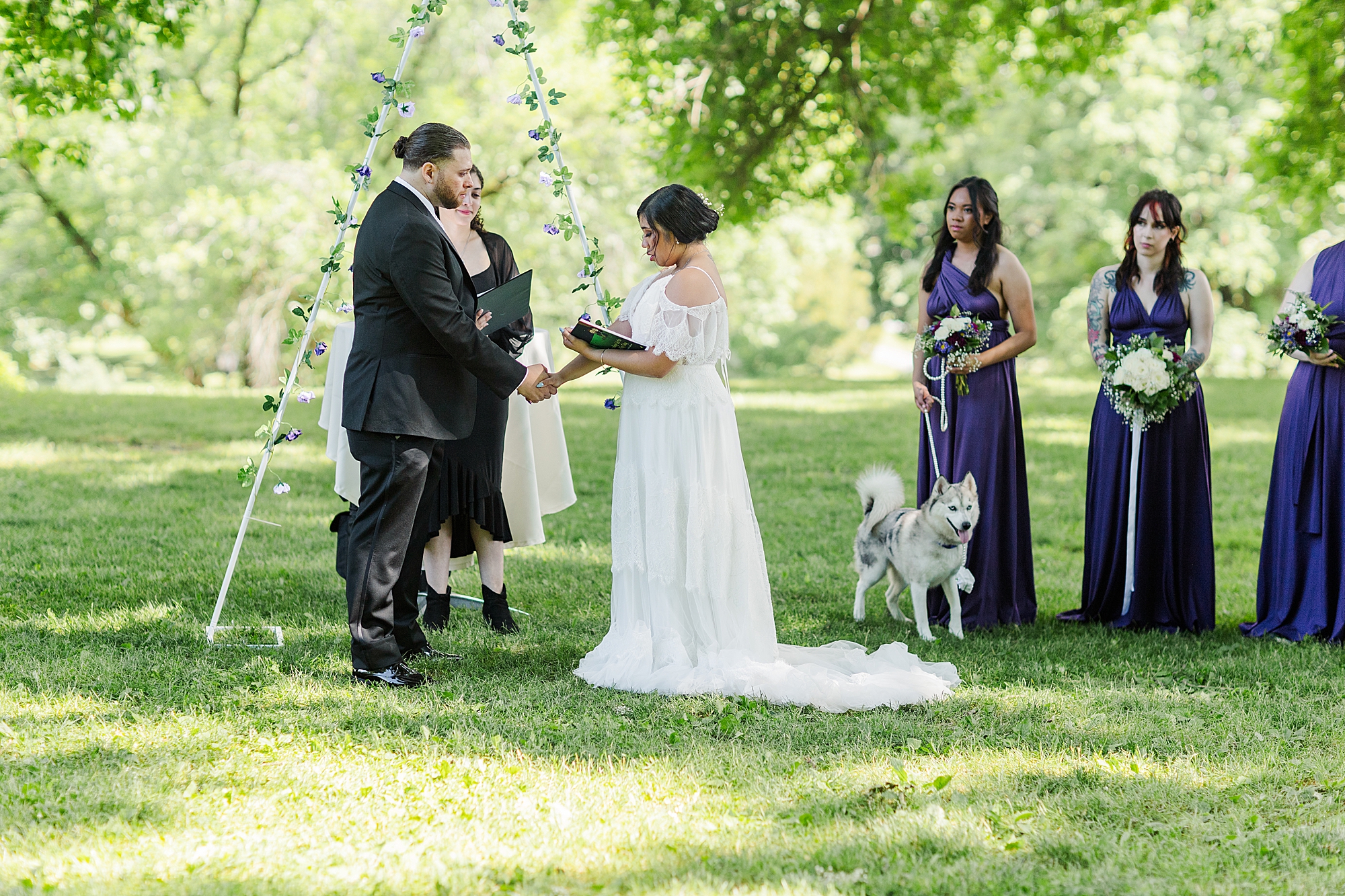 bride holding hands with groom while reading vows and bridesmaids watching 