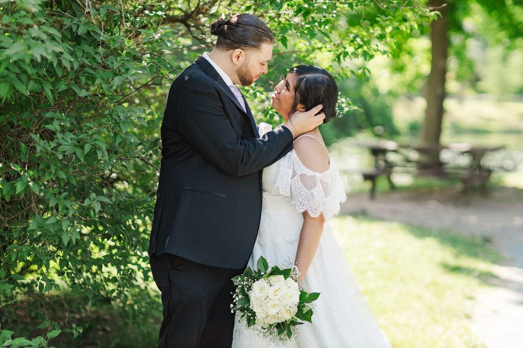 groom holding his bride next to a tree 