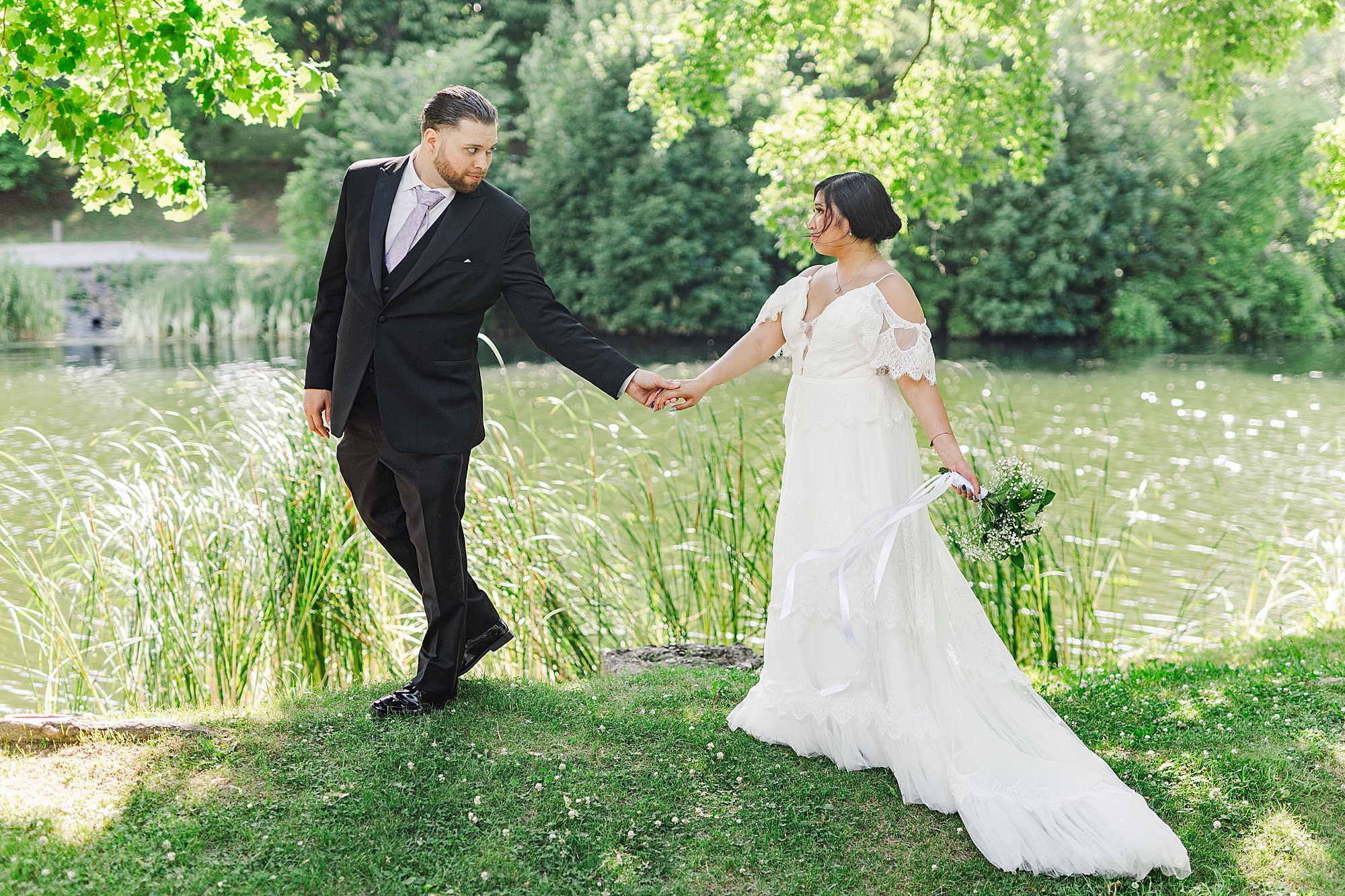 bride and groom holding hands while walking on a hill next to a lake 