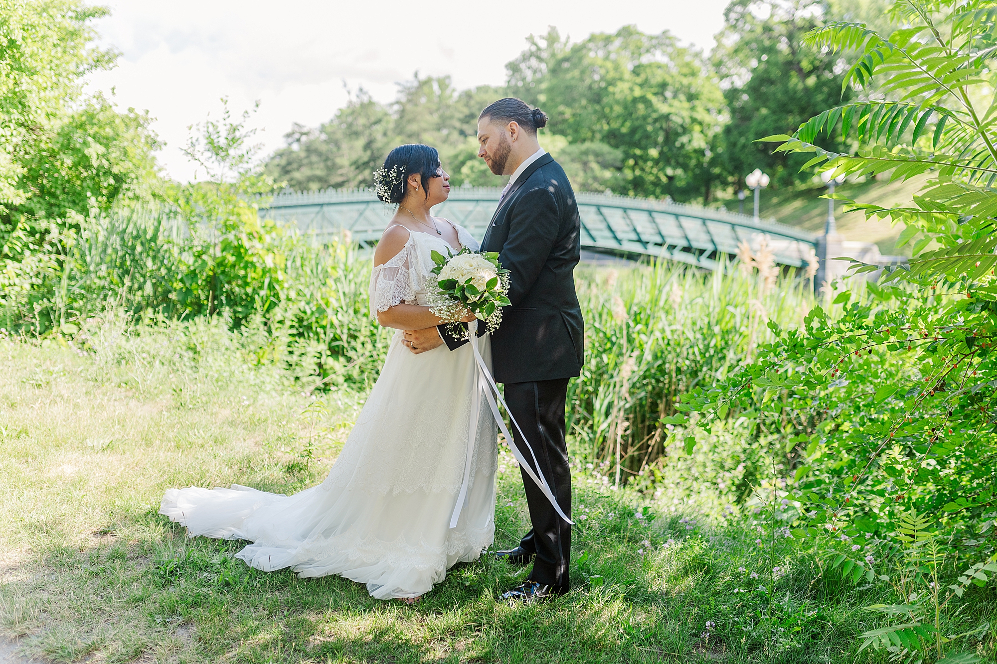 bride and groom looking at each other while standing near a bridge in a park 