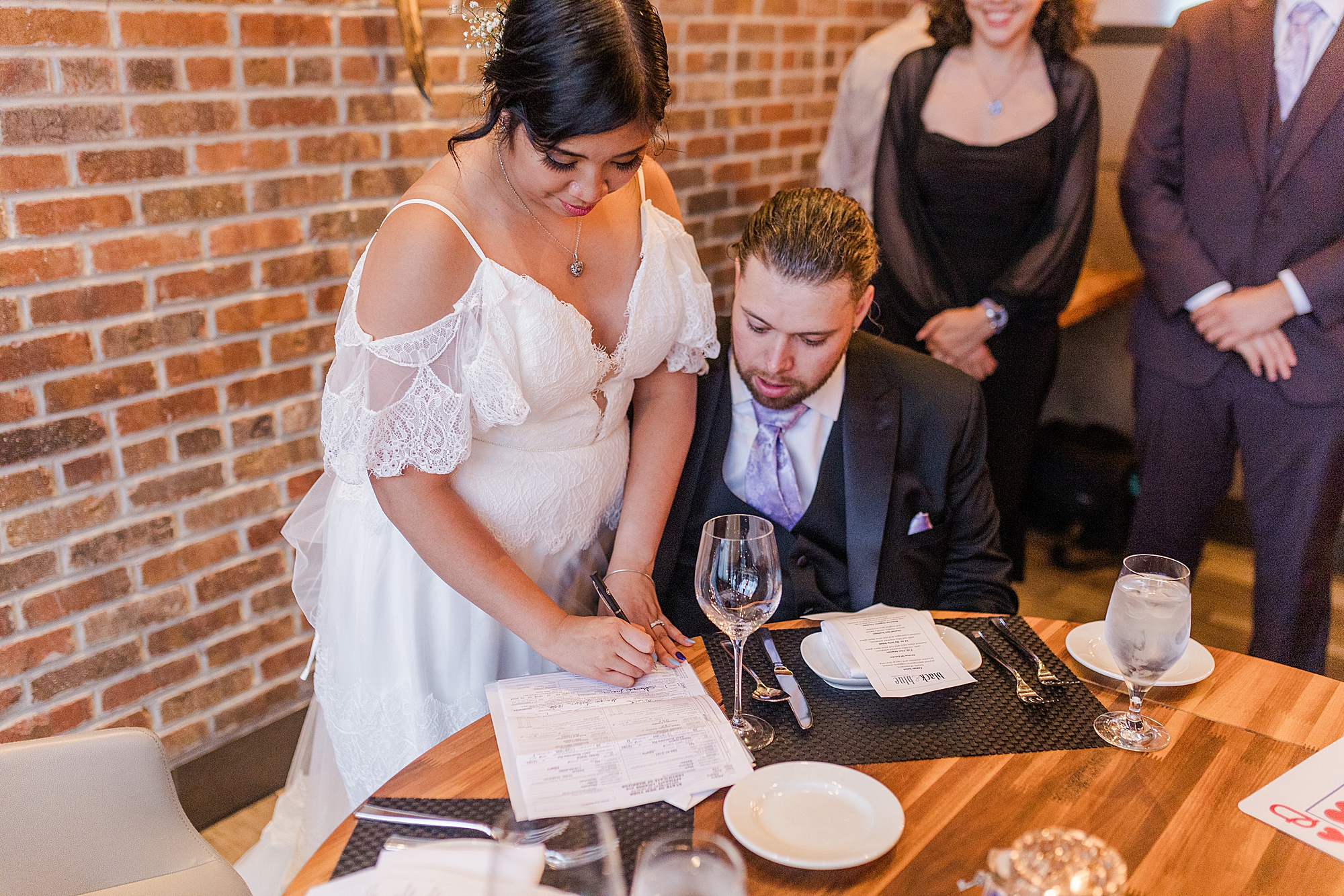 bride and groom signing papers at dinner table 