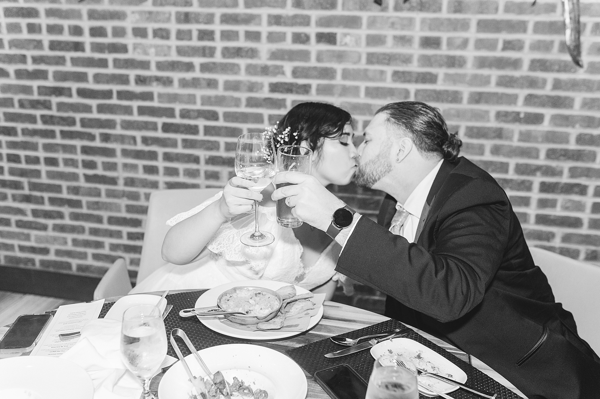 bride and groom making a toast to each other at dinner while sharing a kiss 