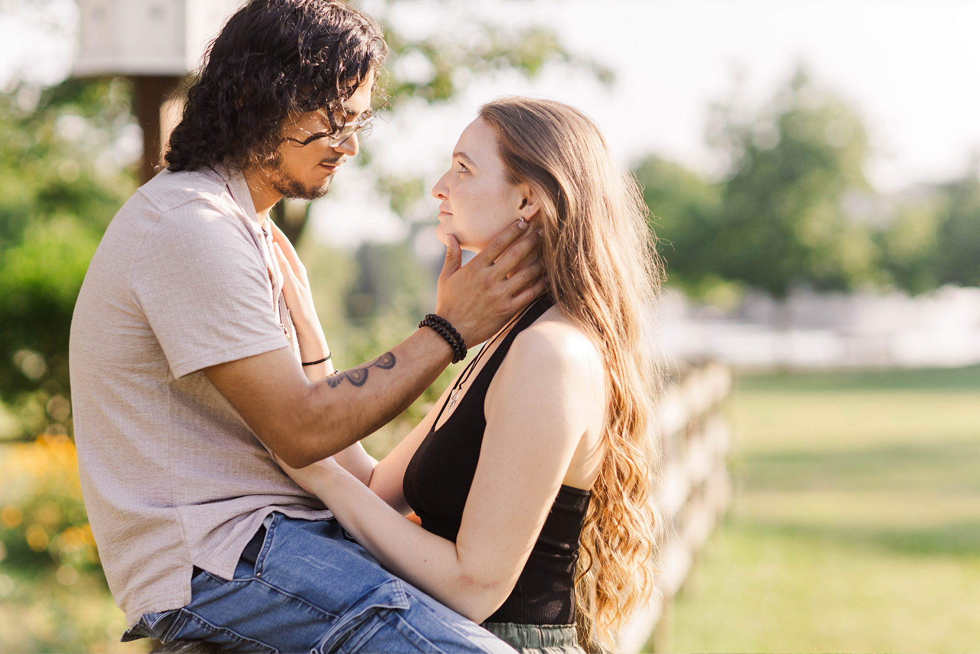 a couple shares a loving stare while the boyfriend is sitting on a fence