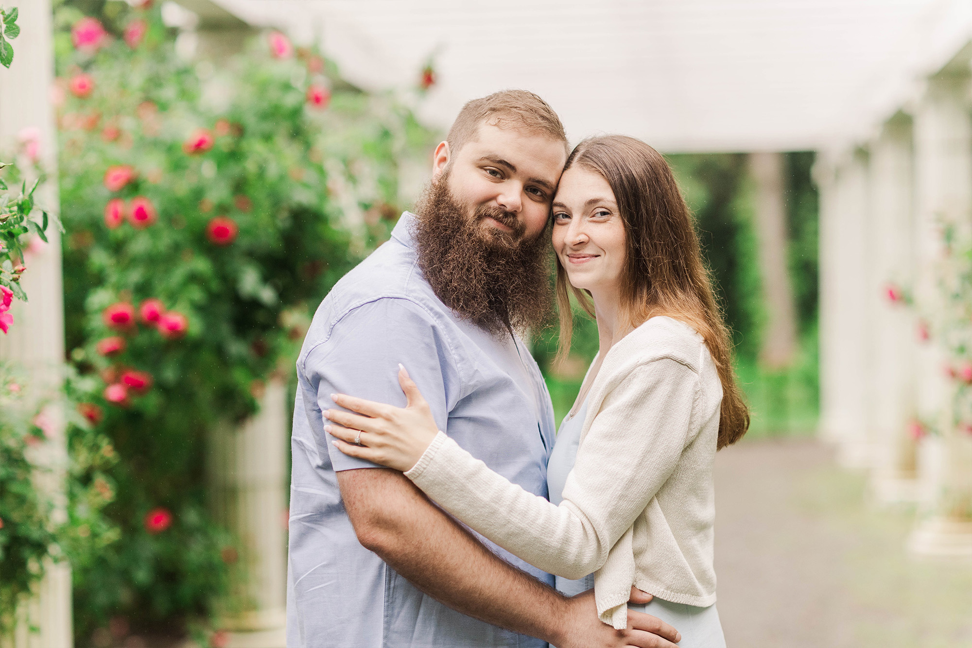 young couple standing under archway with greenery and roses