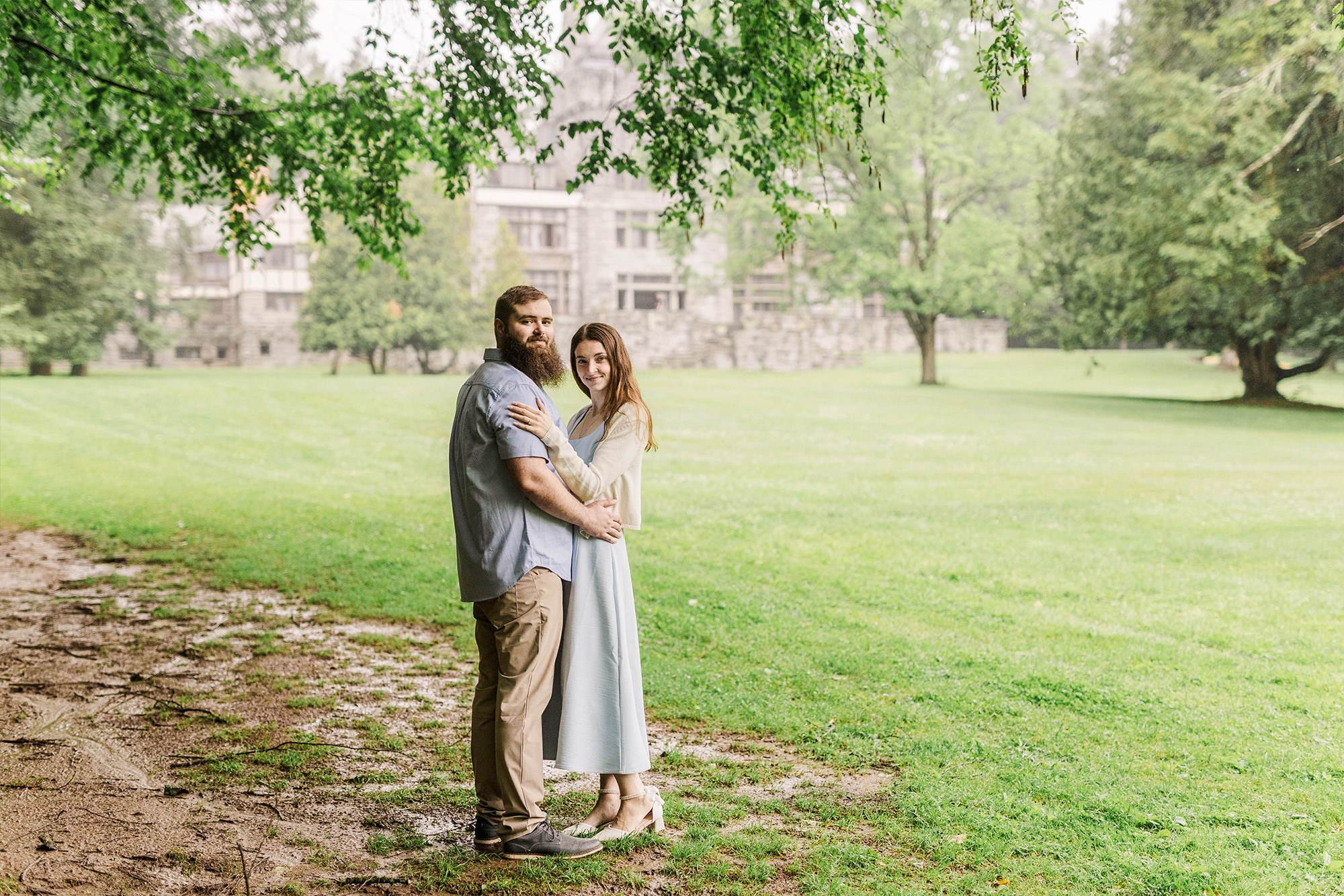 couple holding each other underneath tree with mansion