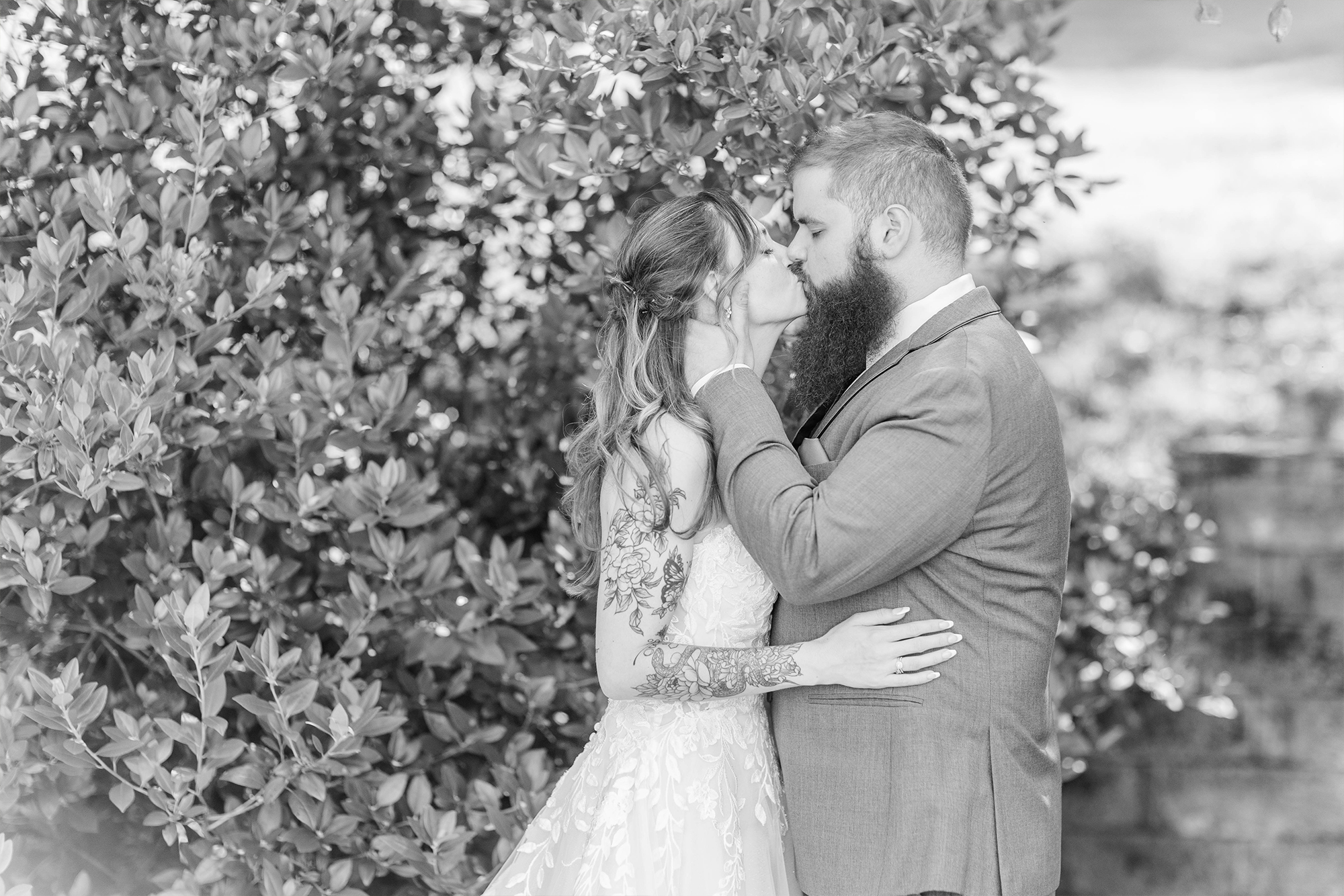 bride and groom sharing a kiss next to large bush