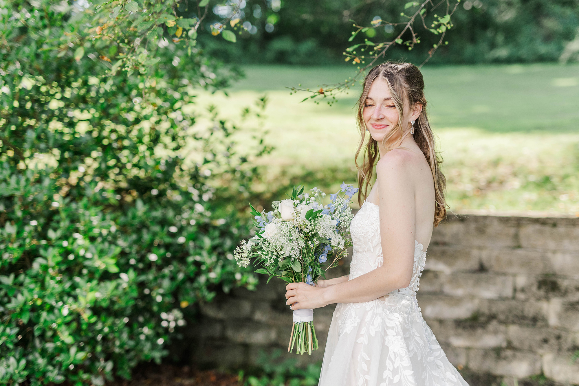bride holding bouquet looking down next to bush