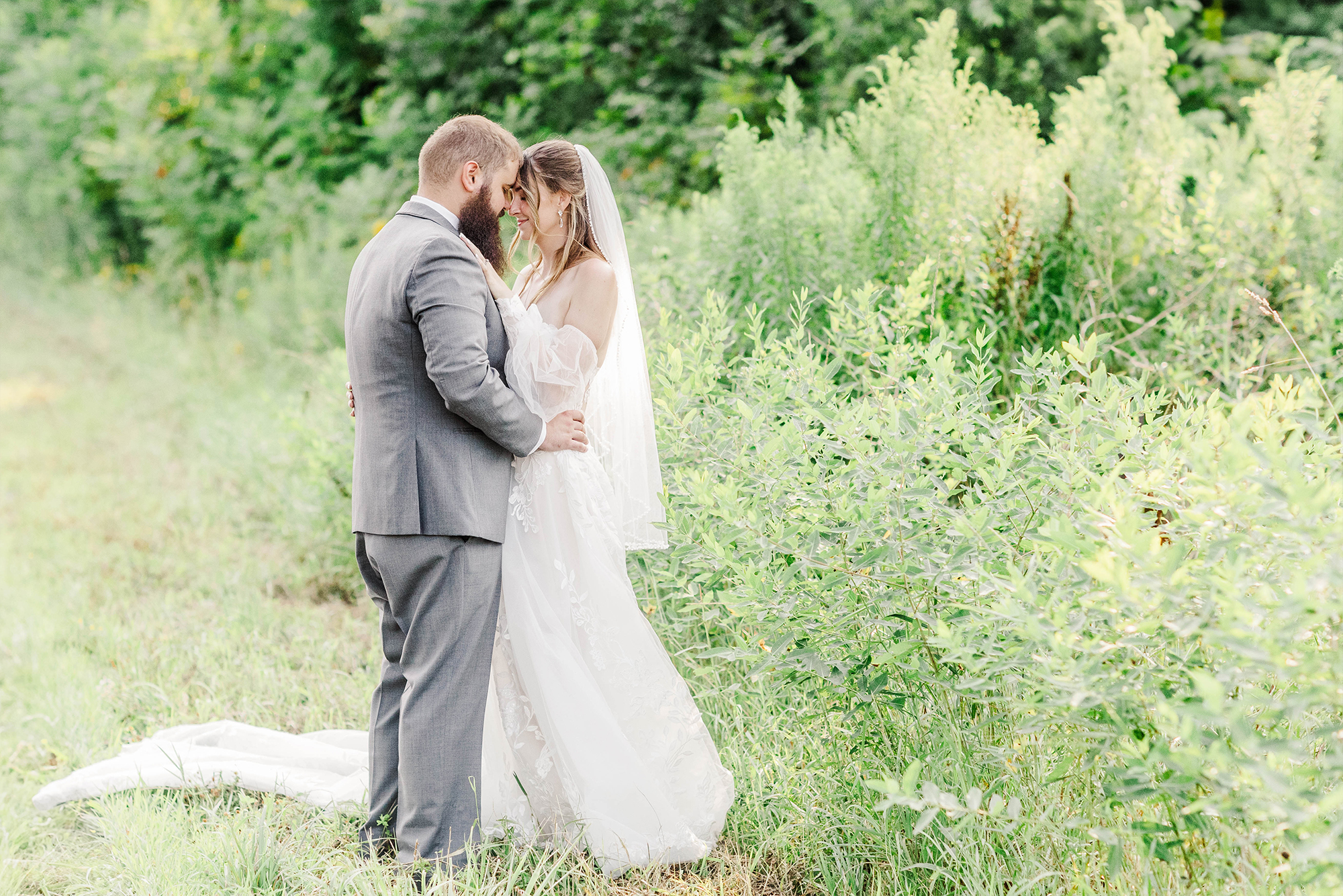 bride and groom touching foreheads with tall greenery