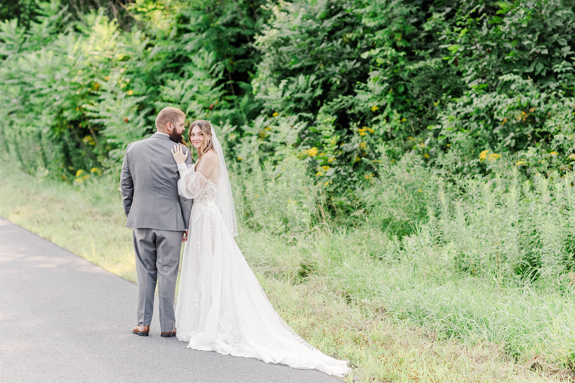 bride and groom standing on road with tall trees