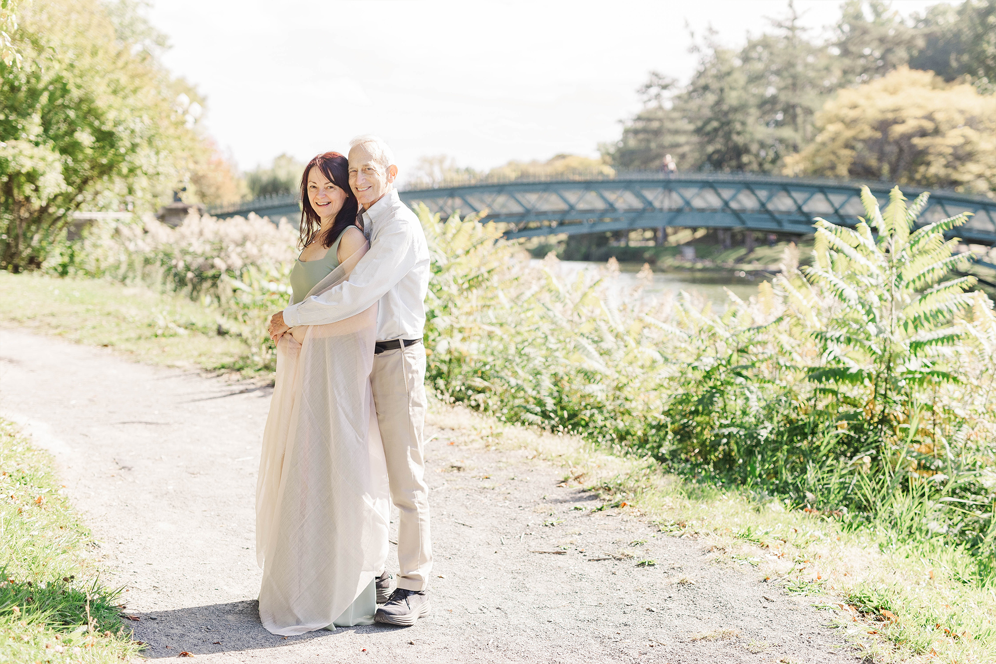 couple holding each other with bridge in park