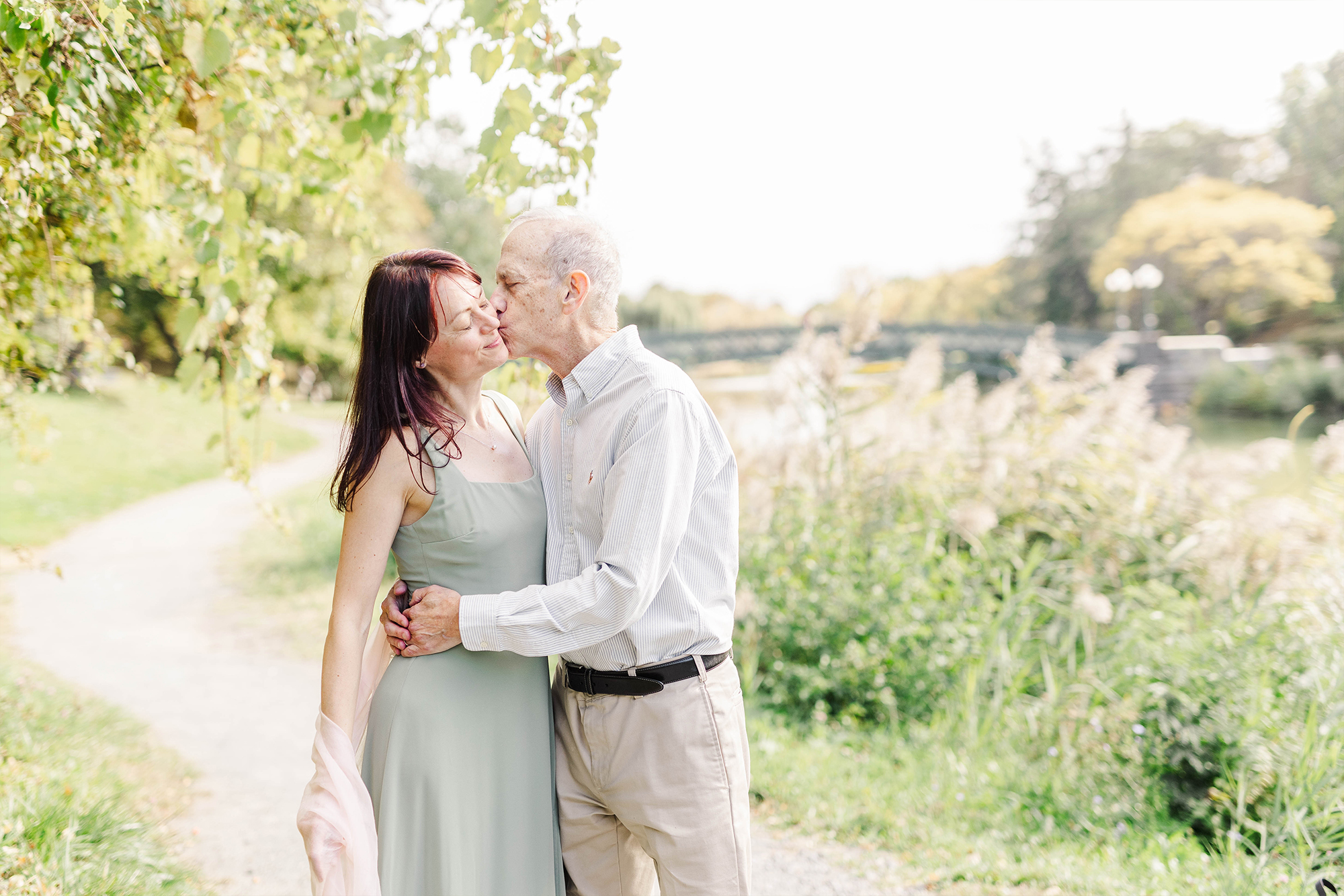 couple sharing kiss in park with tall greenery