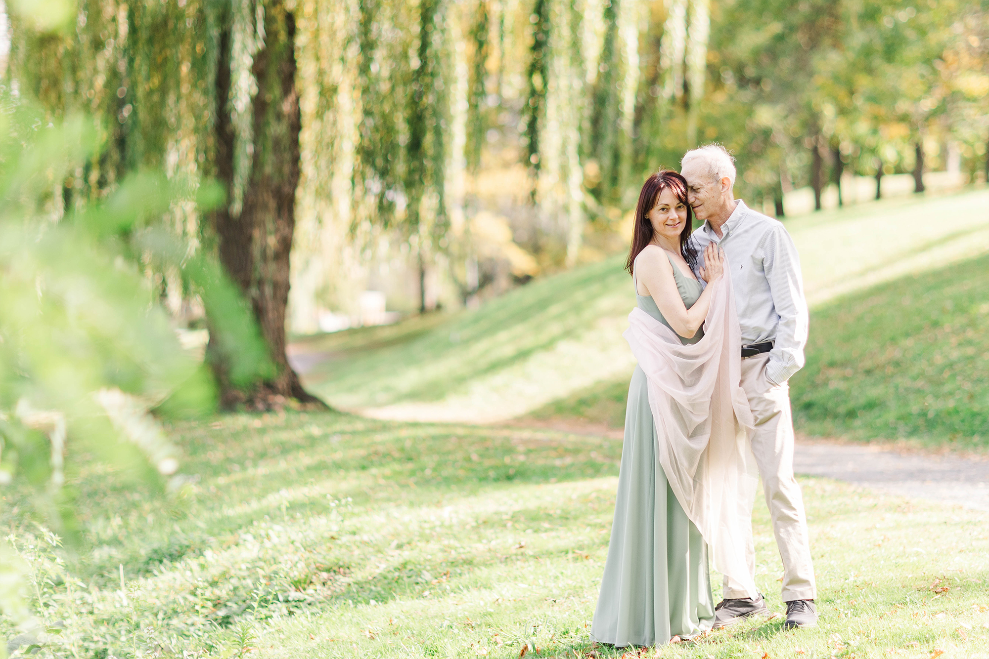 couple embracing each other in front of willow tree in park