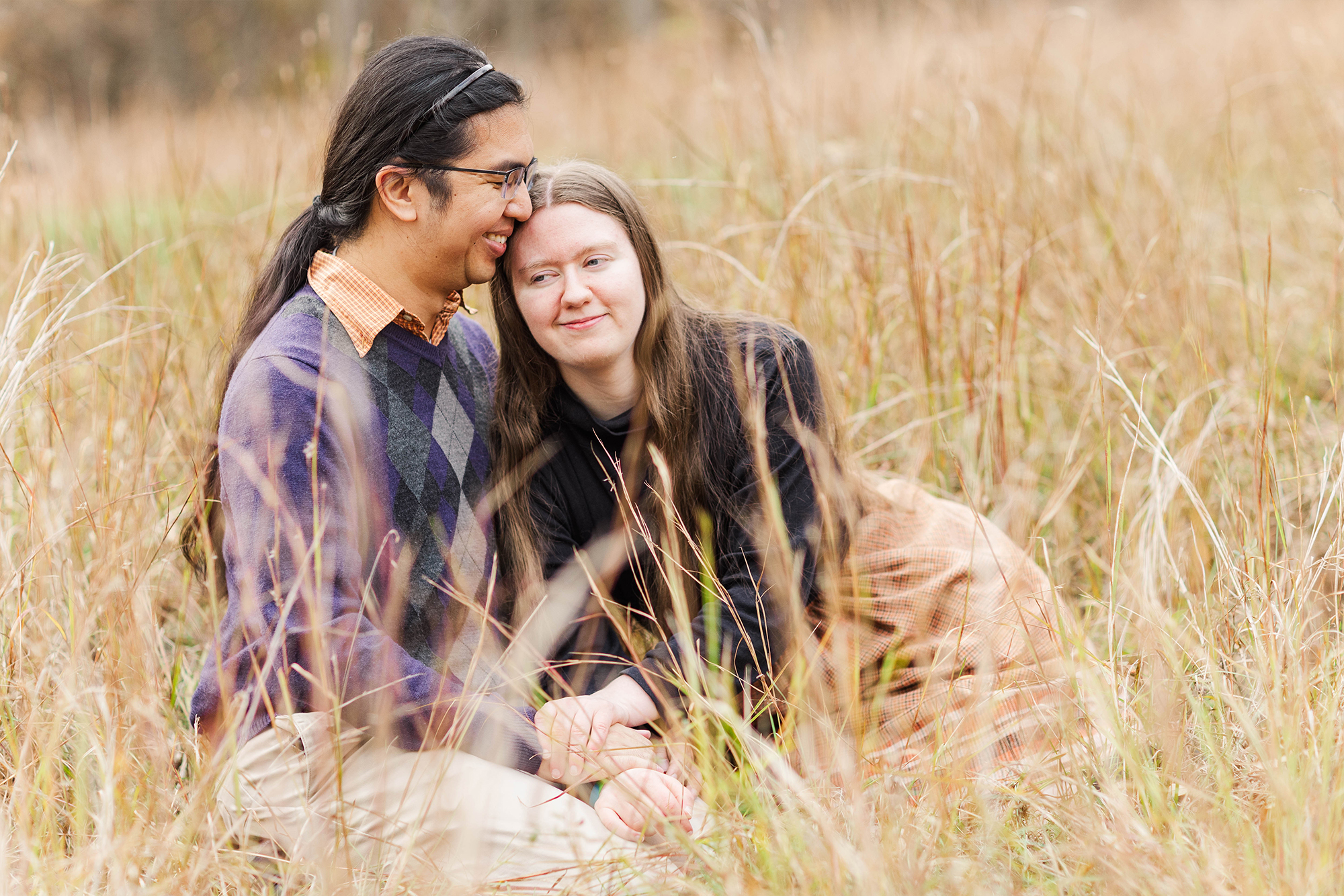 couple sitting in tall grass while one partner leans on the others shoulder