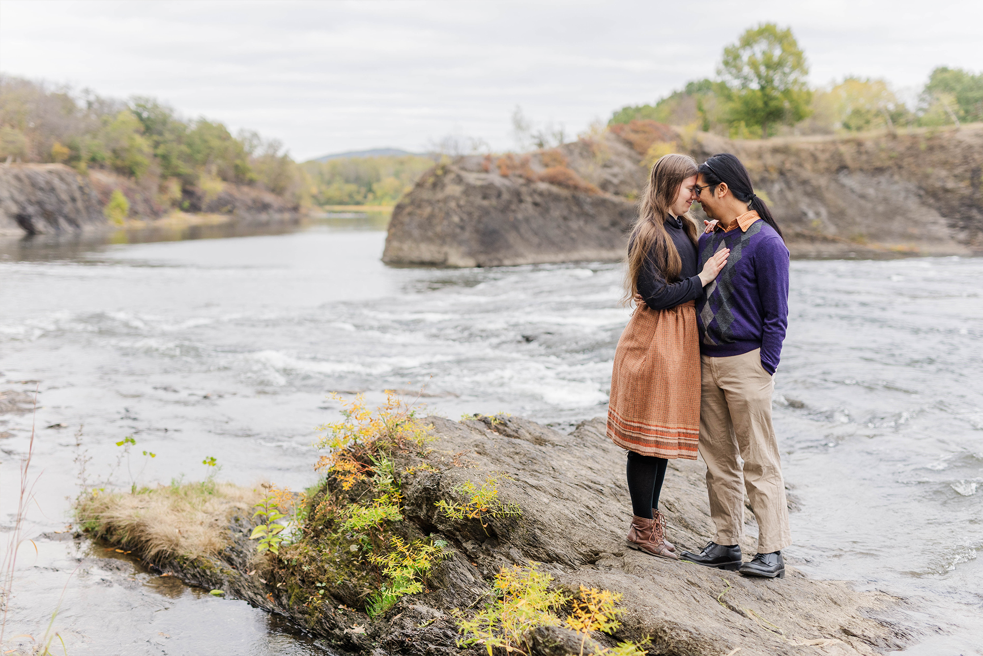 couple resting their foreheads against each other while standing on rocks next to water