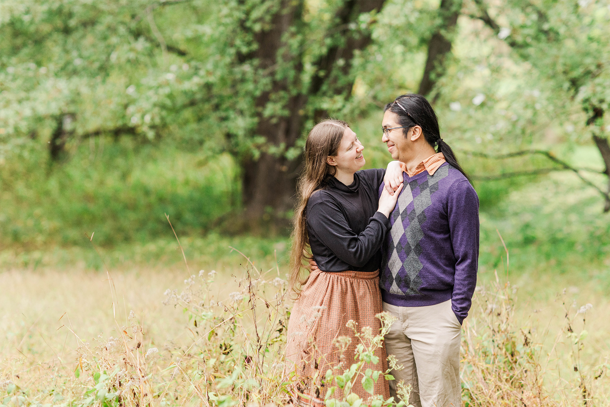 couple sharing soft stare while posing with each other in tall grass with trees