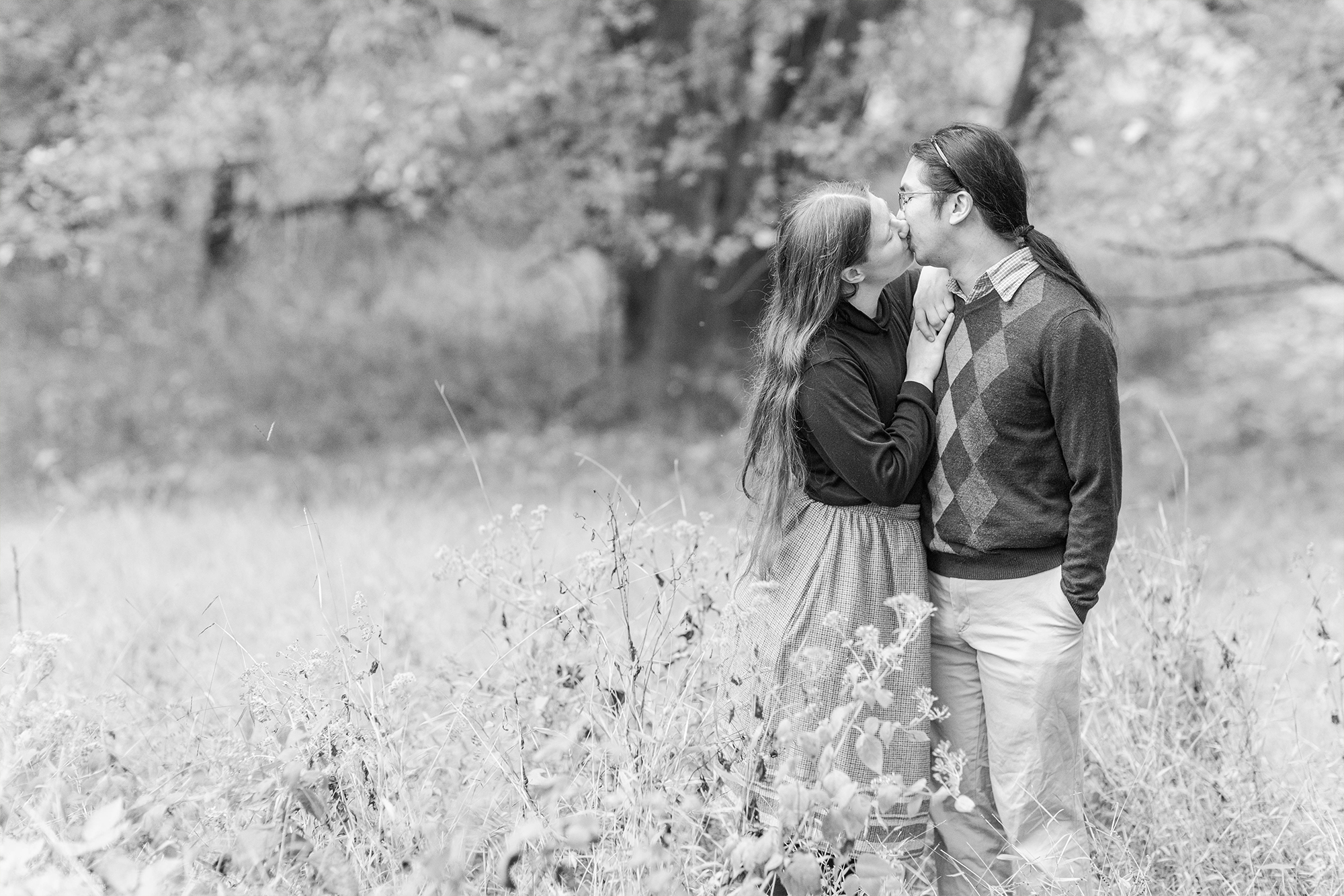 couple sharing kiss in park surrounded by tall trees