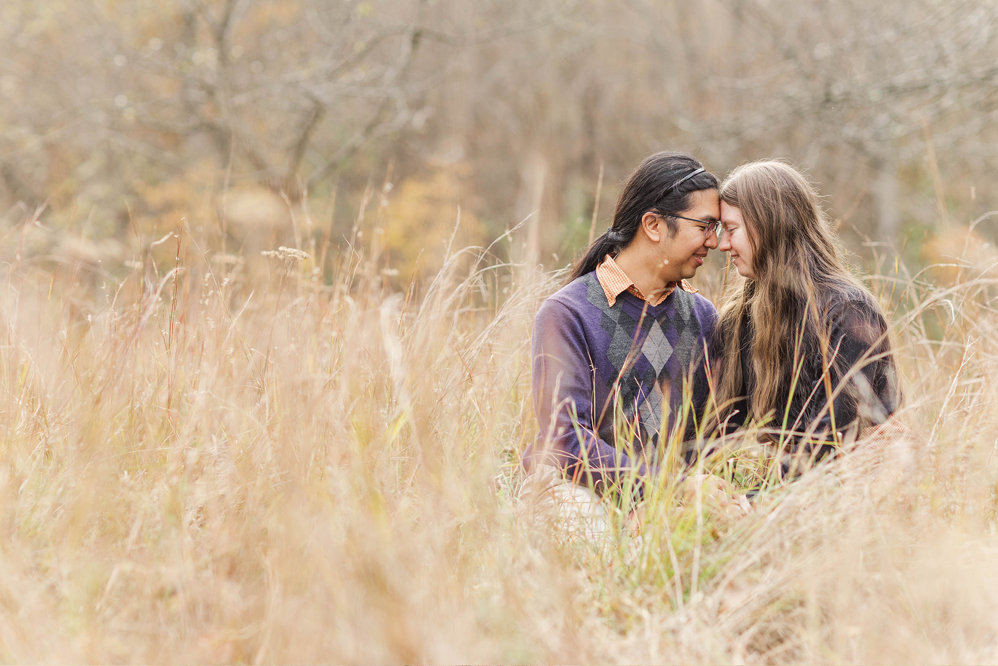 couple sitting in tall grass with foreheads pressing against each other