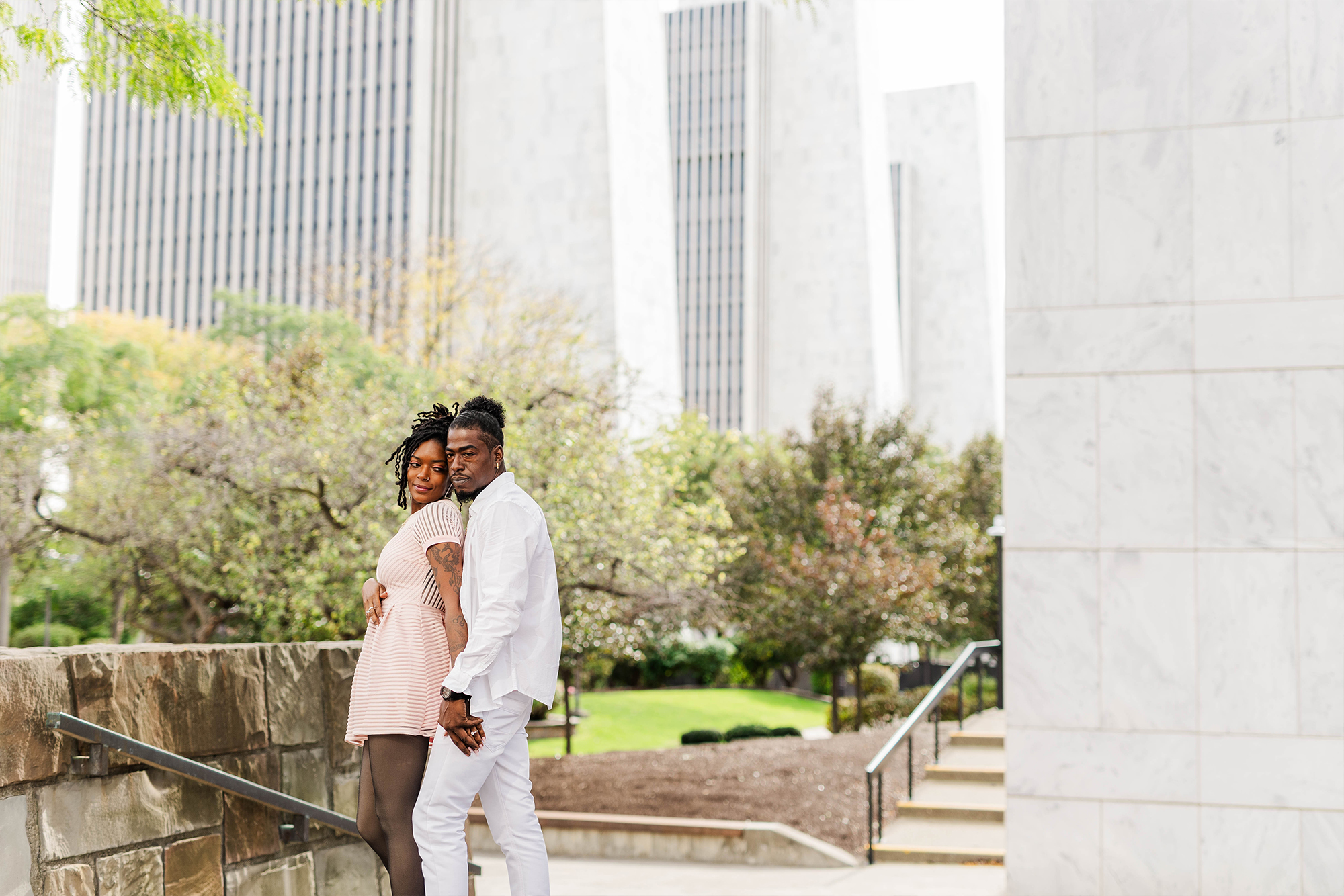 couple posing with each other in front of park with city buildings