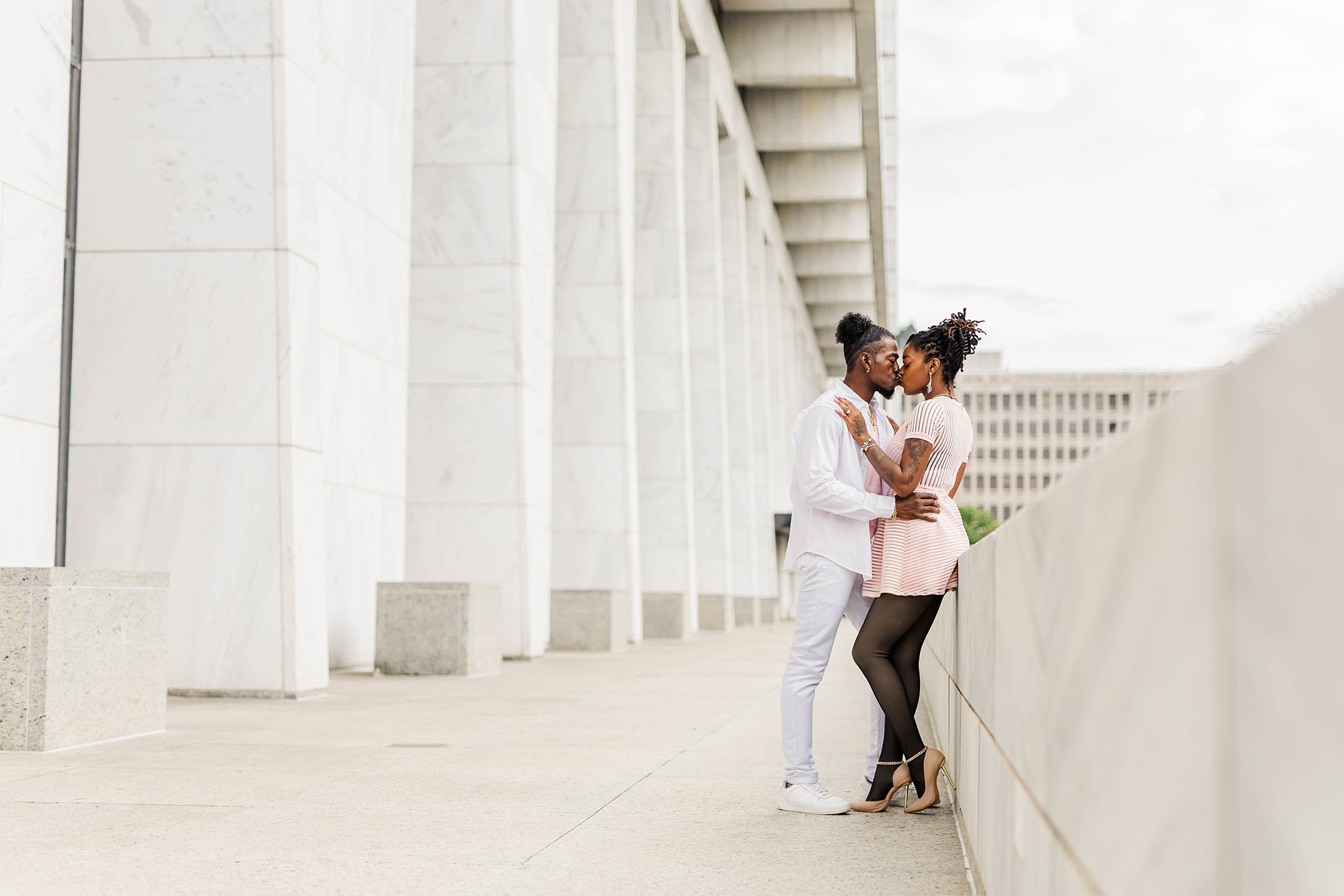 couple sharing kiss while leaning against wall in front of architectual building
