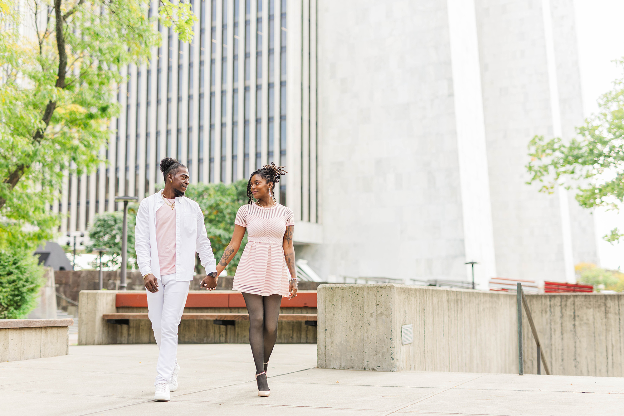 couple walking hand in hand in park with office building and greenery