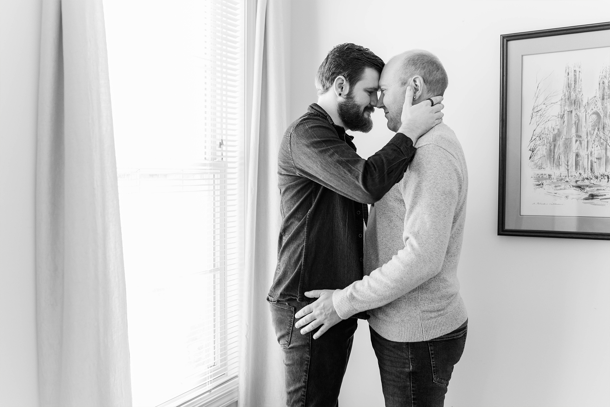 couple holds each other with foreheads pressed while standing next to window