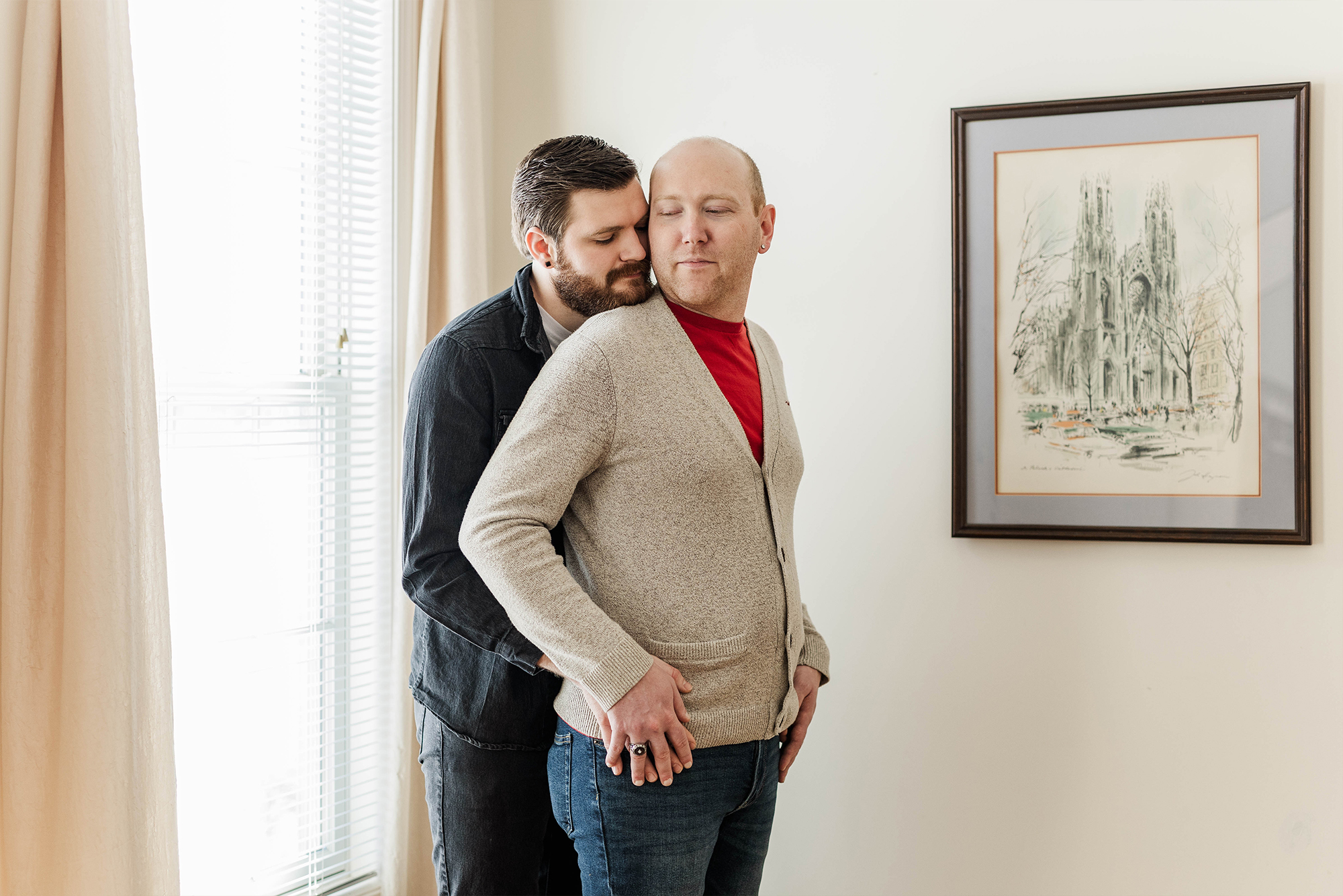 man holds his partner from the back and partner holds onto his hands in sun filled room