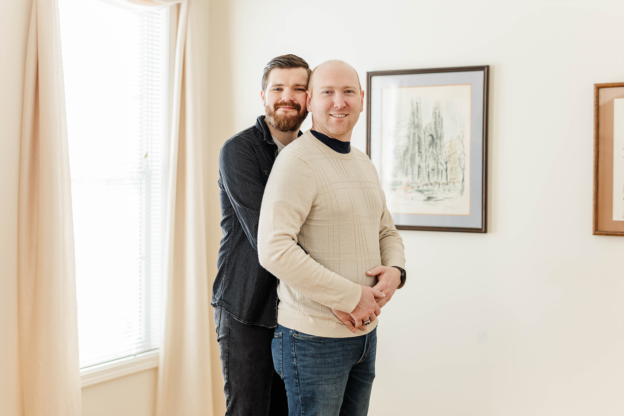Man wrapping his arms around another man in sun filled room