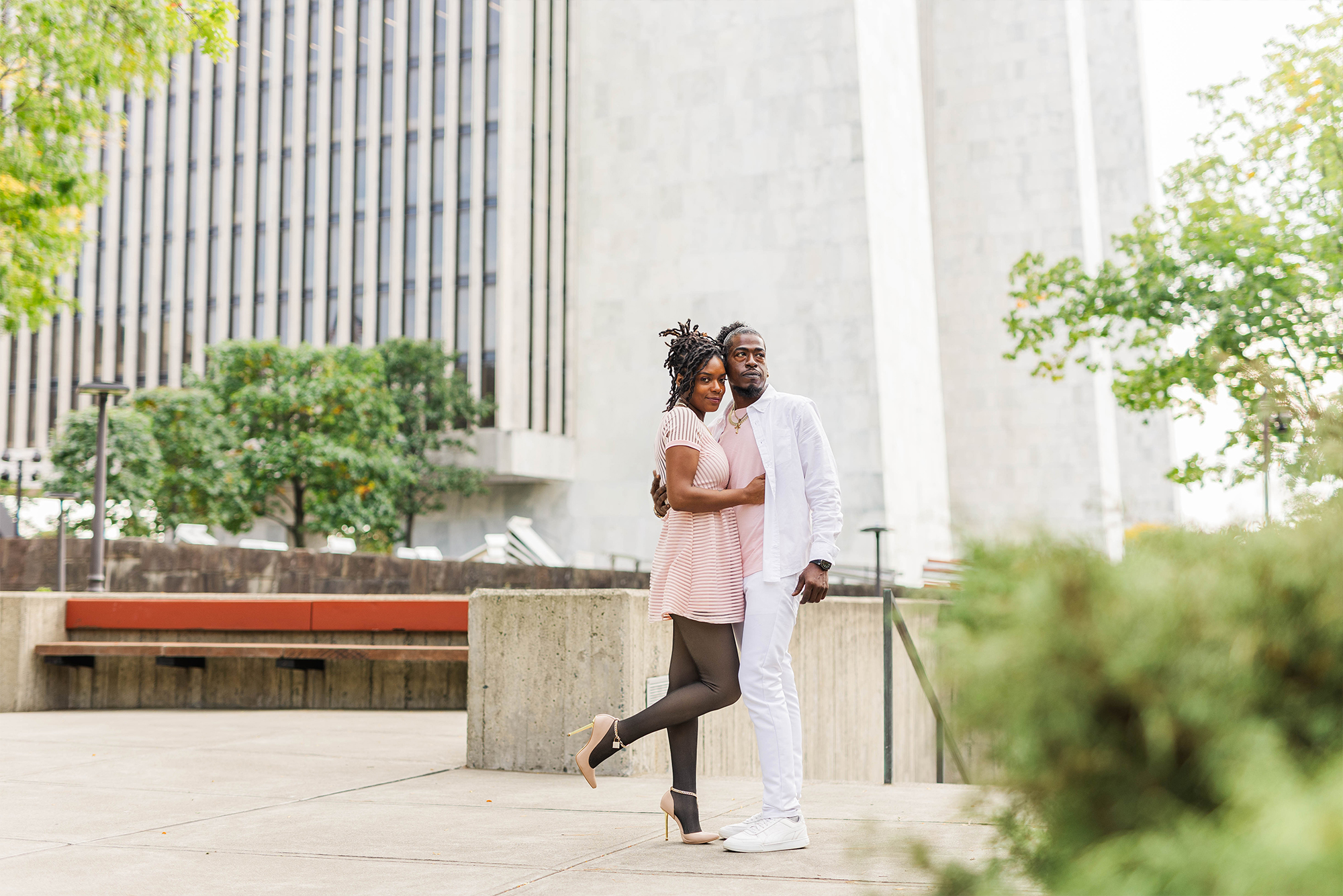 engaged couple in small park with greenery and bushes with buildings