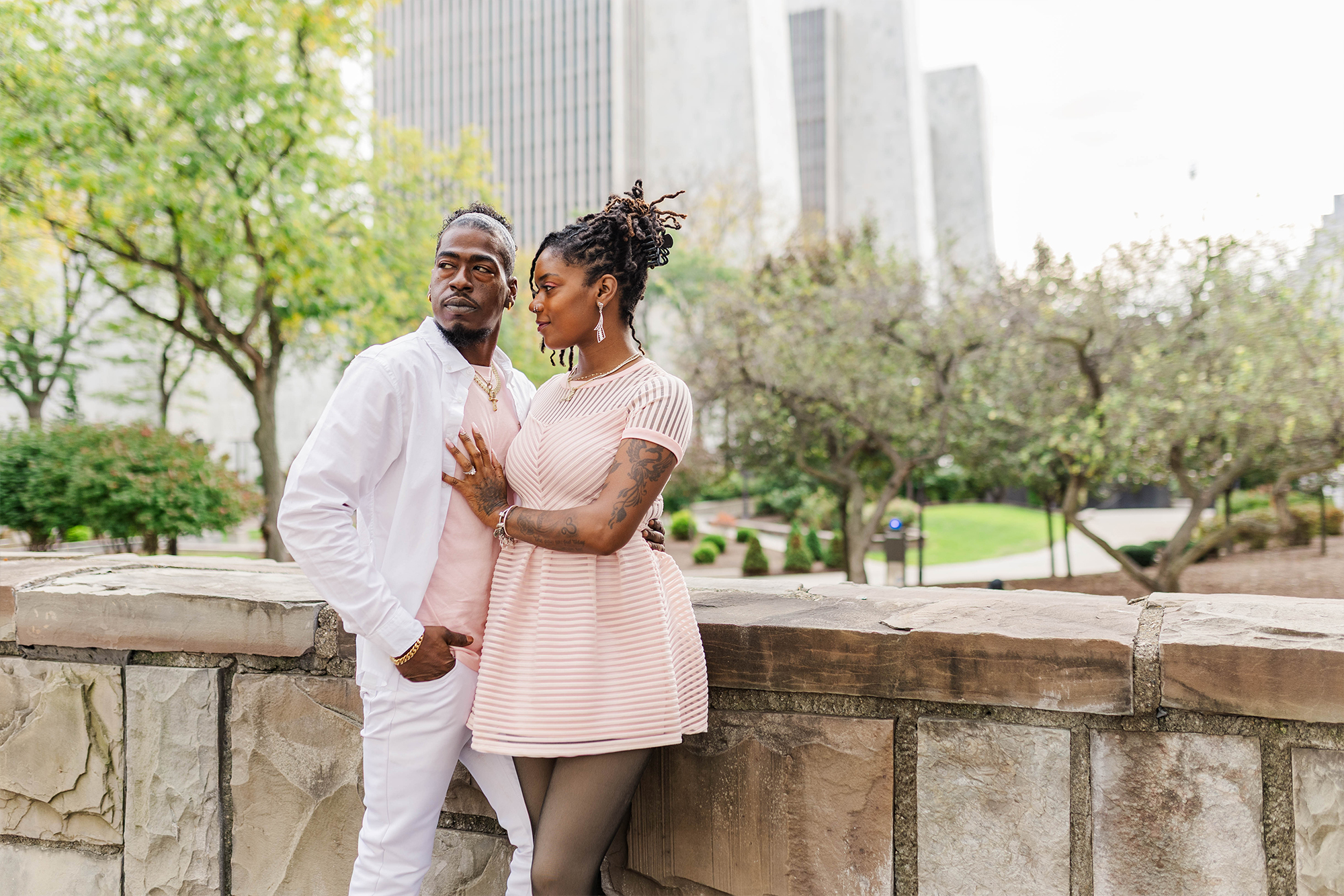 engaged couple posing together in park with trees and buildings