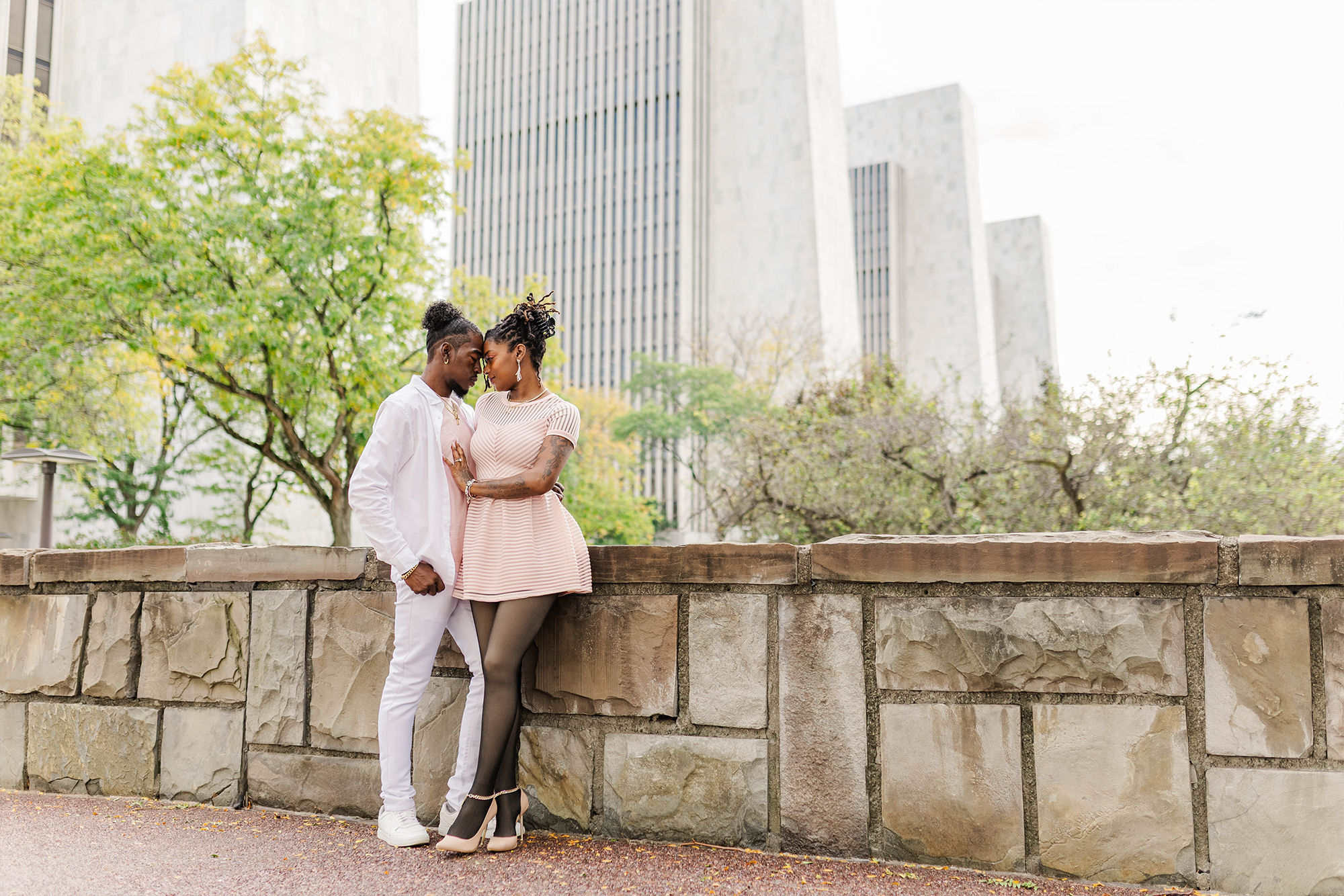 engaged couple with heads pressed against each other with balcony and city backdrop with trees
