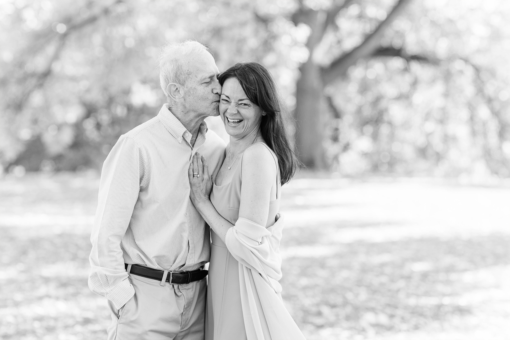 couple laughing together in park in front of large tree