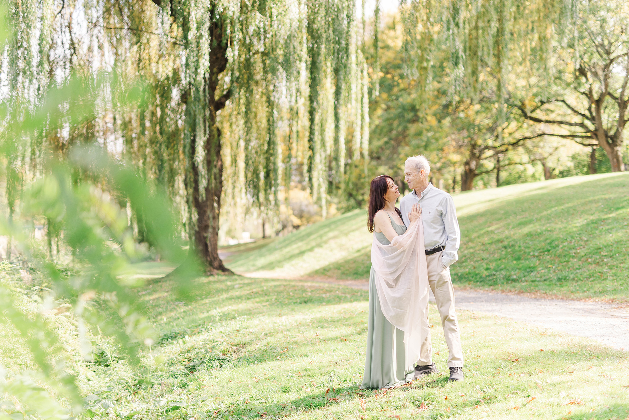 couple posing together in front of large willow tree in park