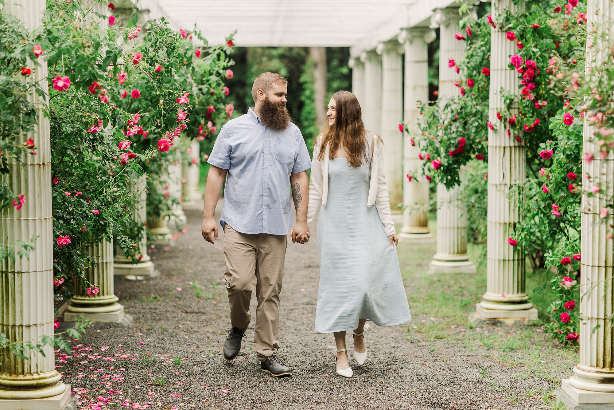 couple walking hand in hand in garden archway with roses and pillars
