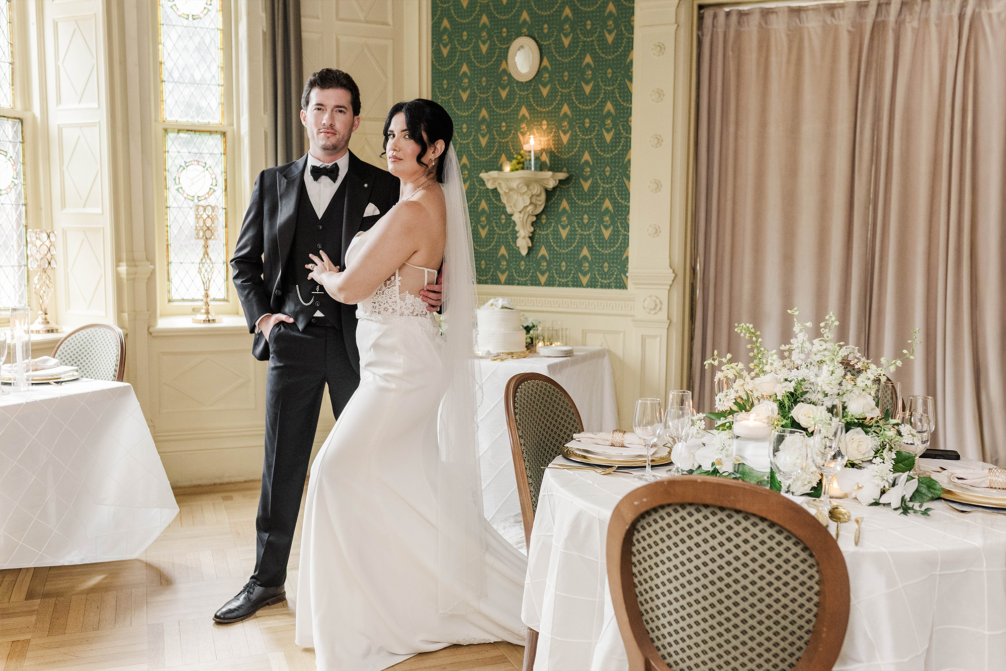 bride and groom posing with each other in dining room with flowers, cake and candles