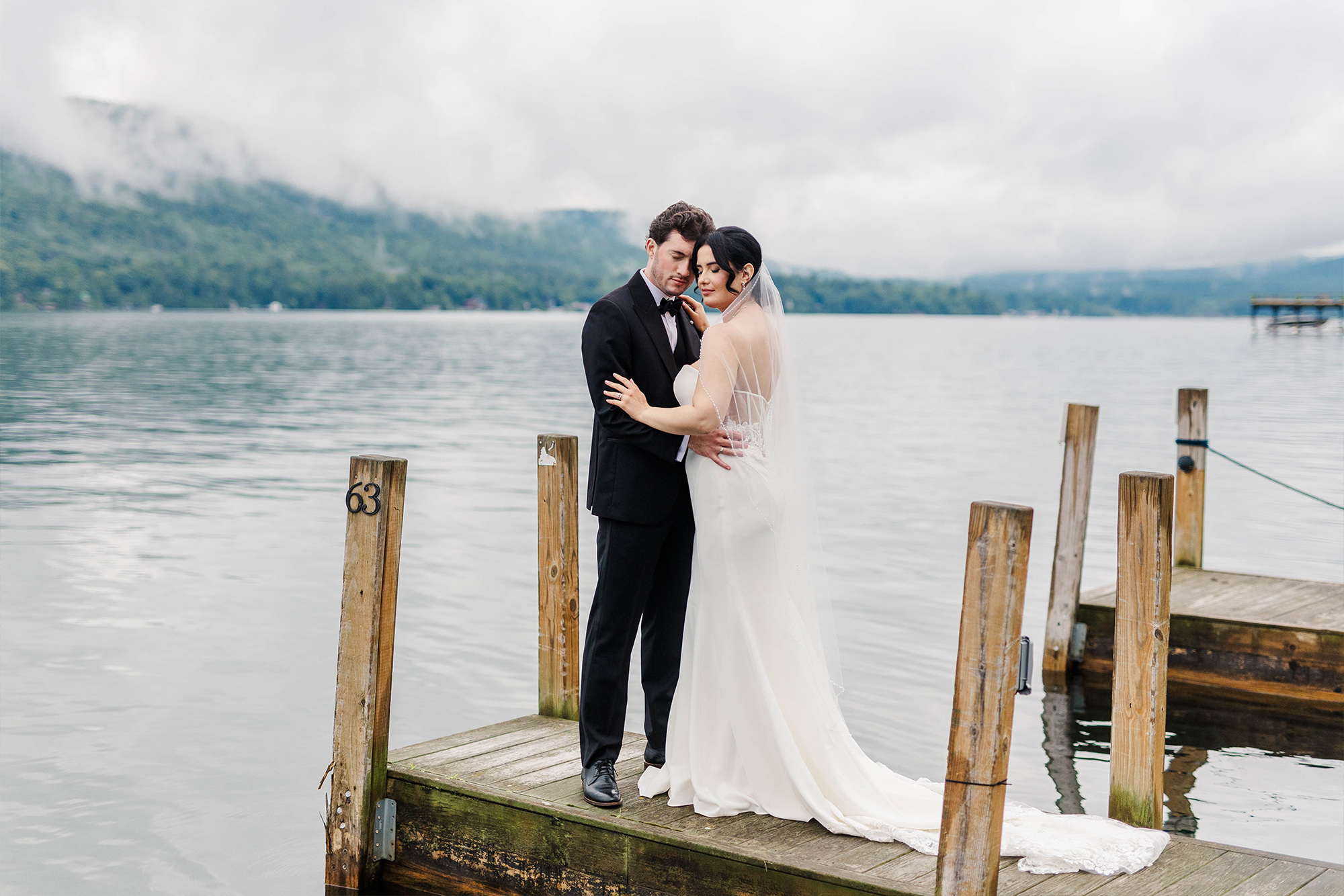 bride and groom embracing on boating dock with lake landscape backdrop on a foggy day