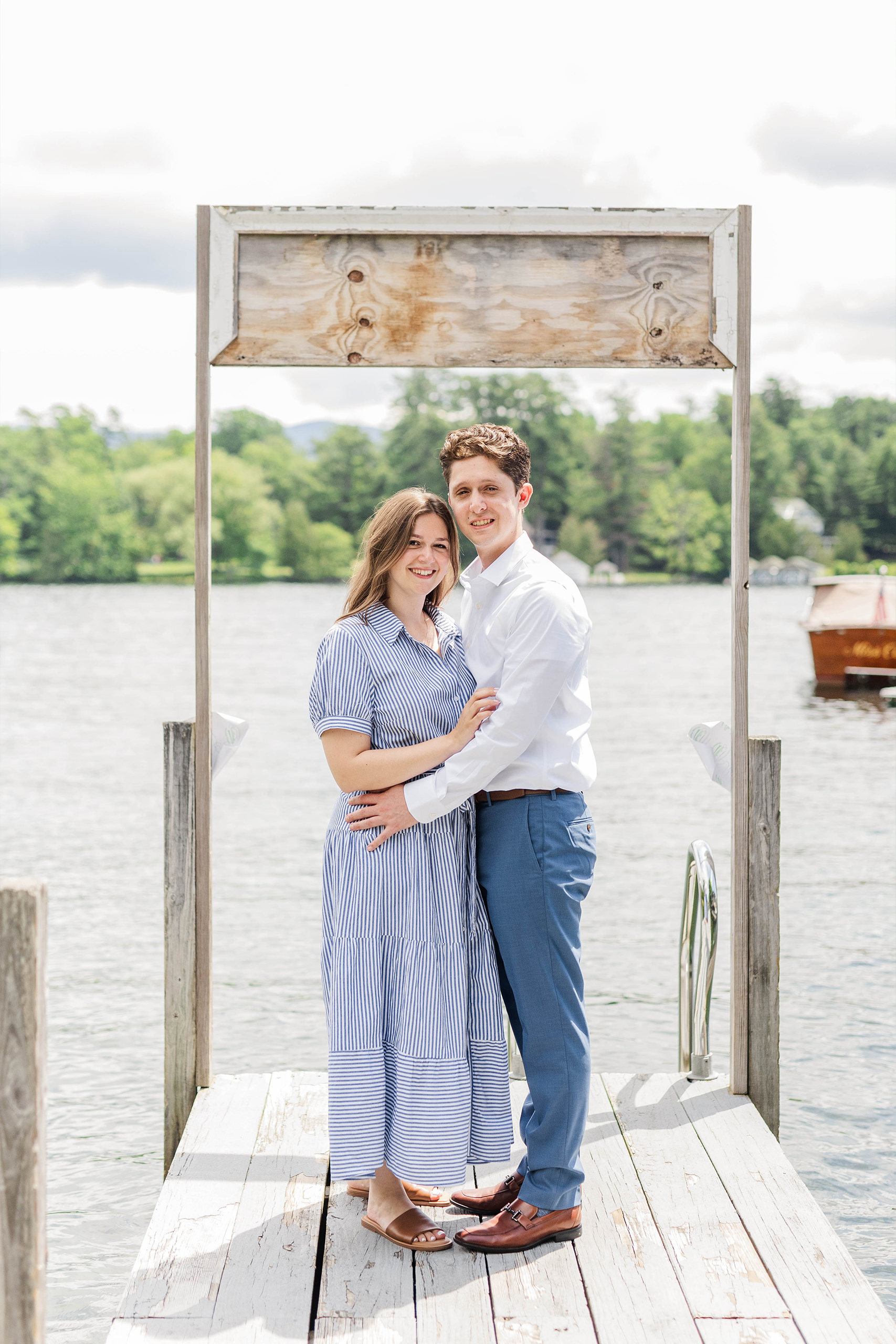 engaged couple standing on dock in front of lake back drop