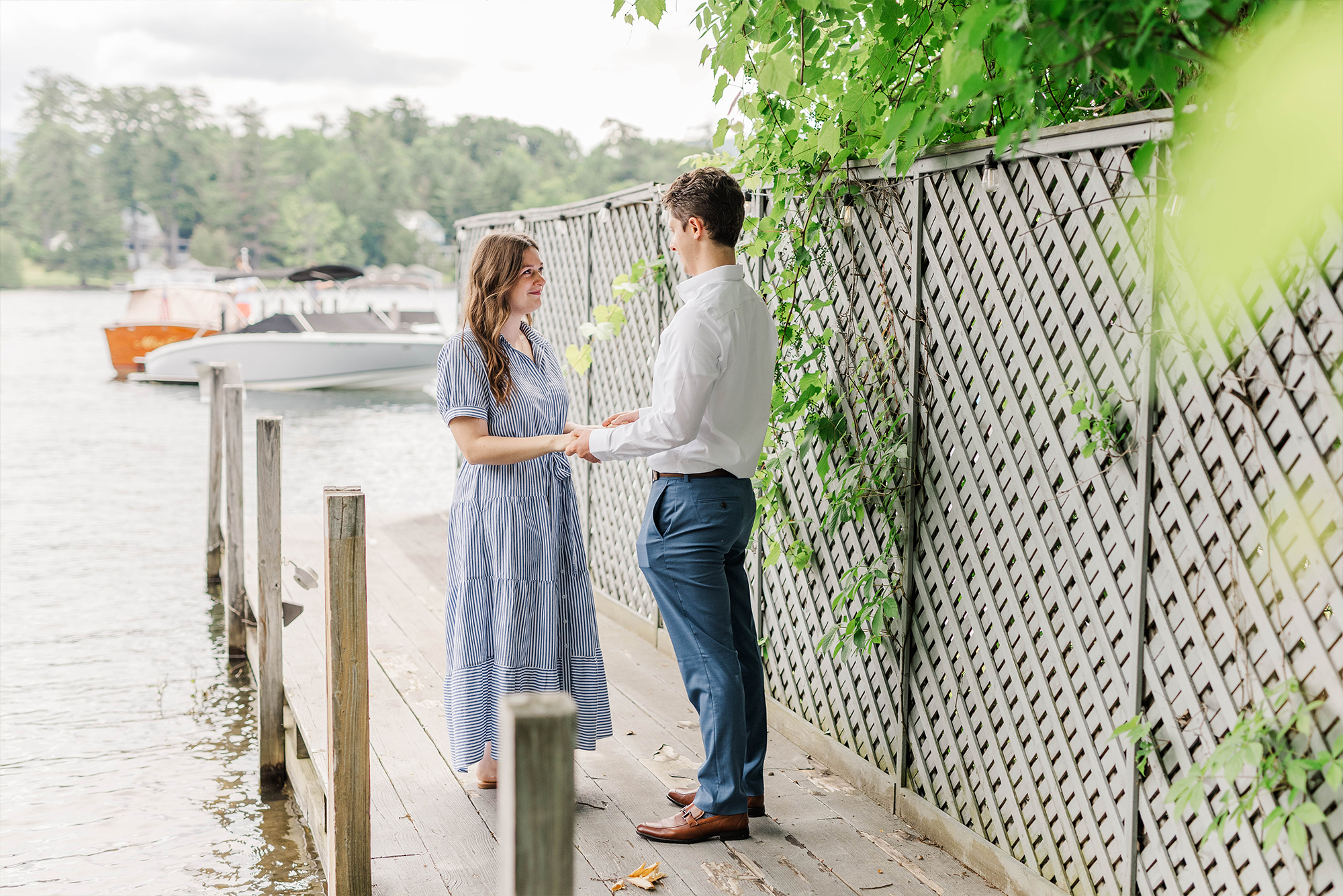 boyfriend proposing to girlfriend on dock with greenery and lake back drop with boat