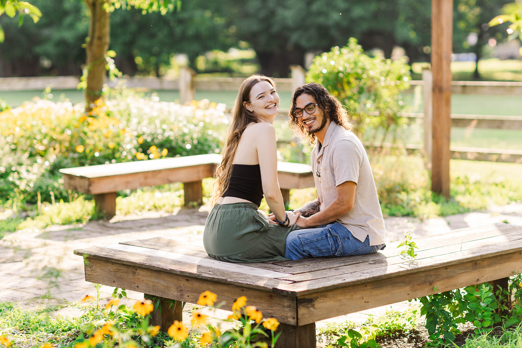 young couple sitting on bench laughing surrounded by flowers in small garden