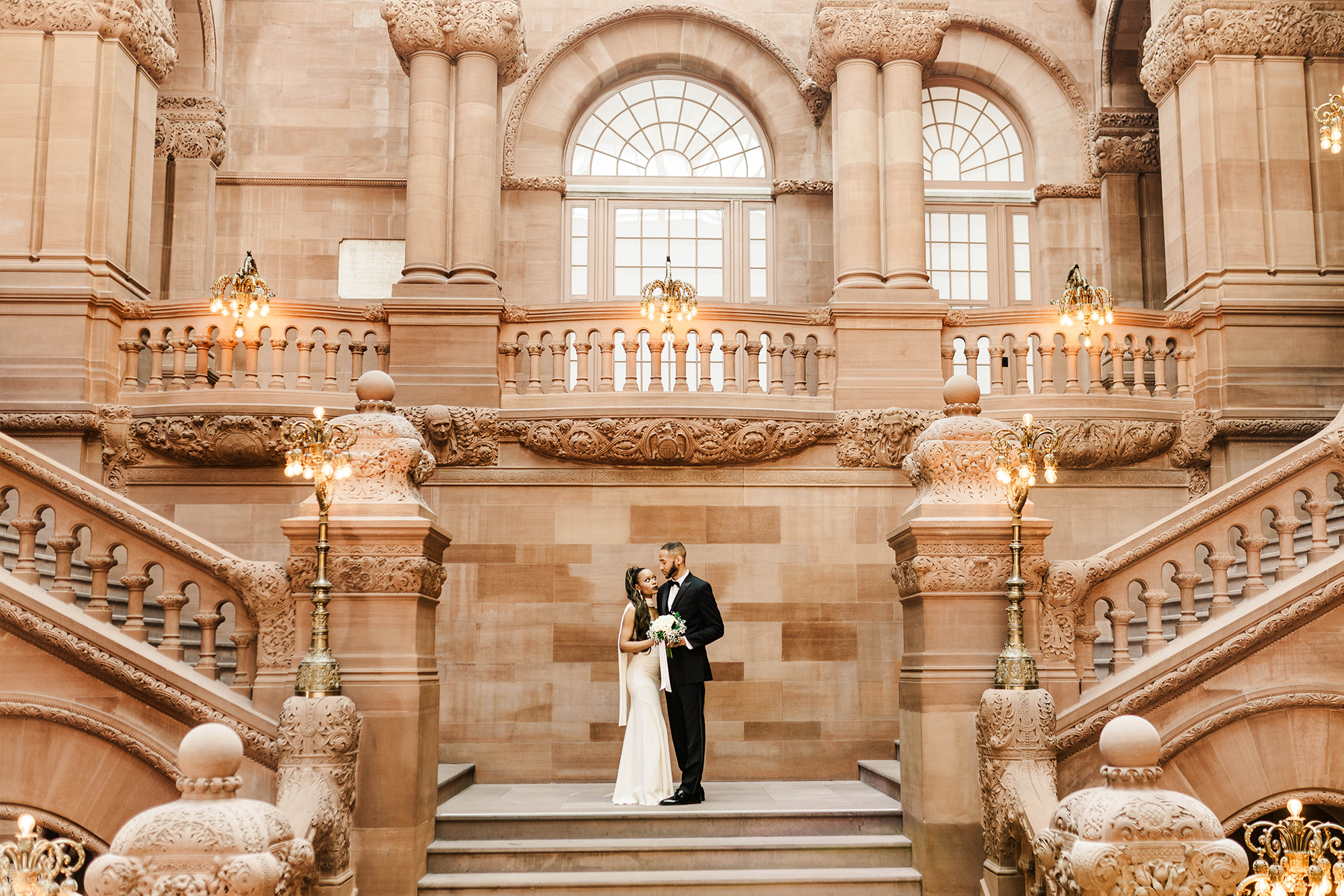 birde and groom posing on large indoor stone grand staircase