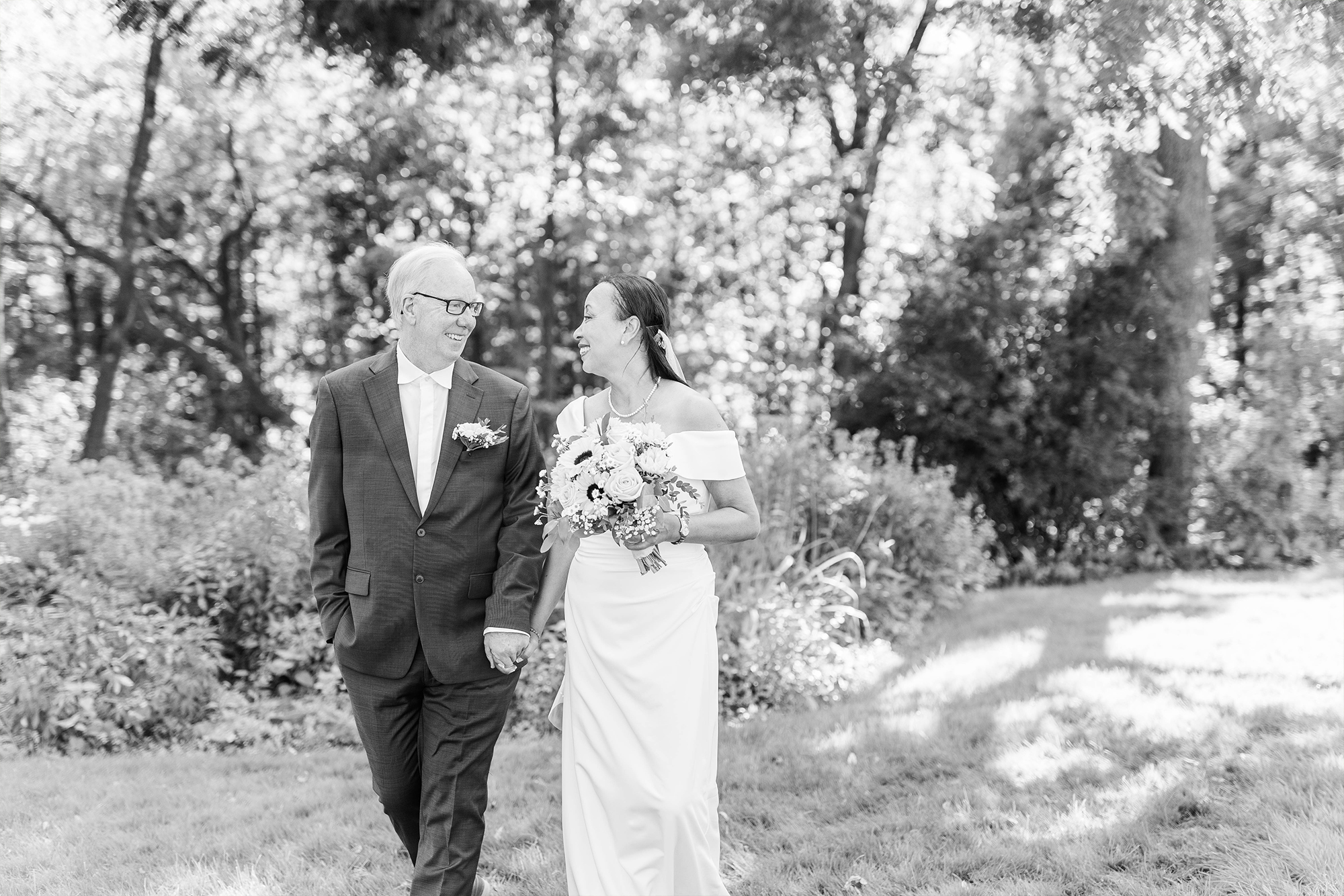 bride and groom walking hand in hand on lawn with tall greenery