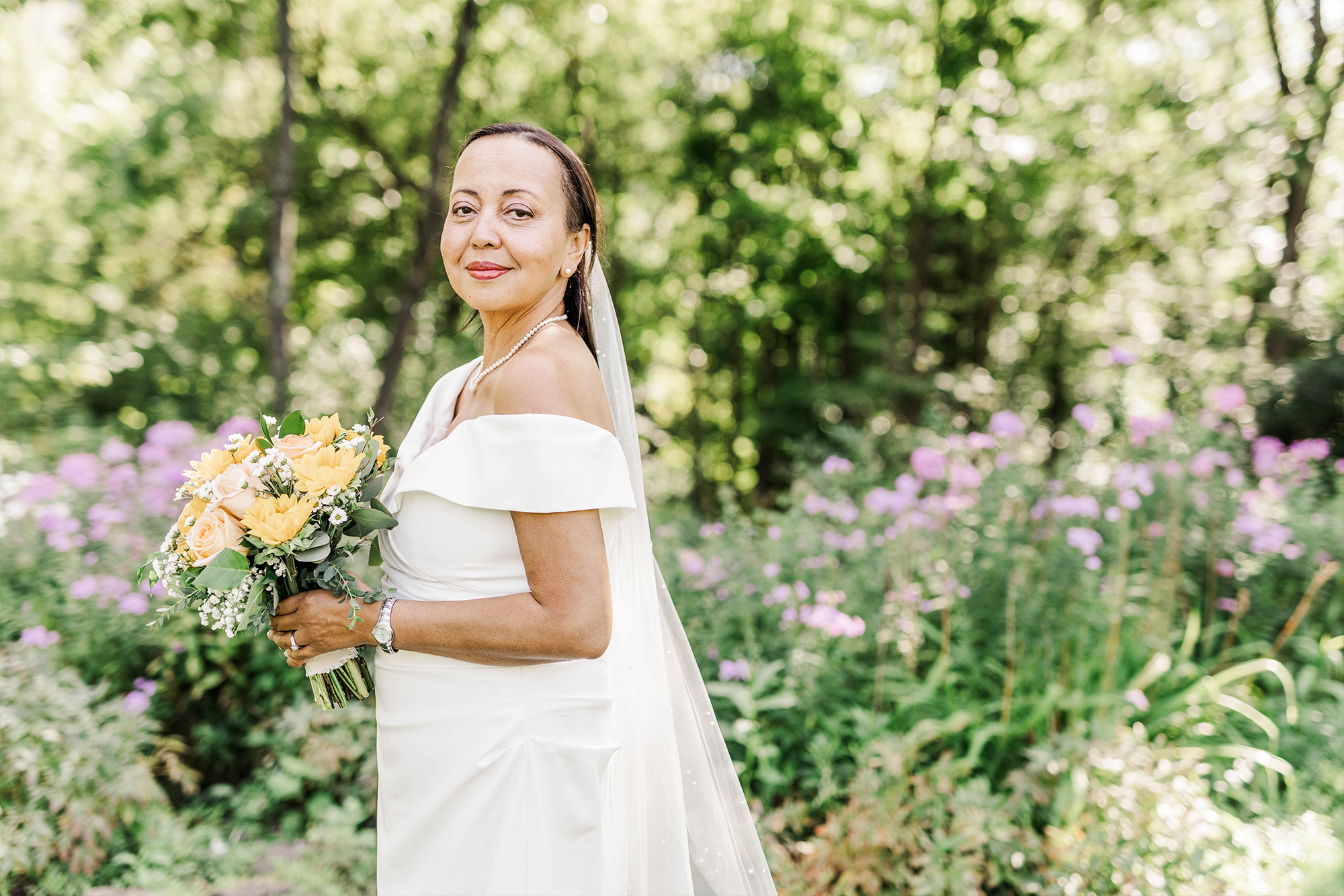 solo bridal portrait with flower bouquet in front of tall greenery