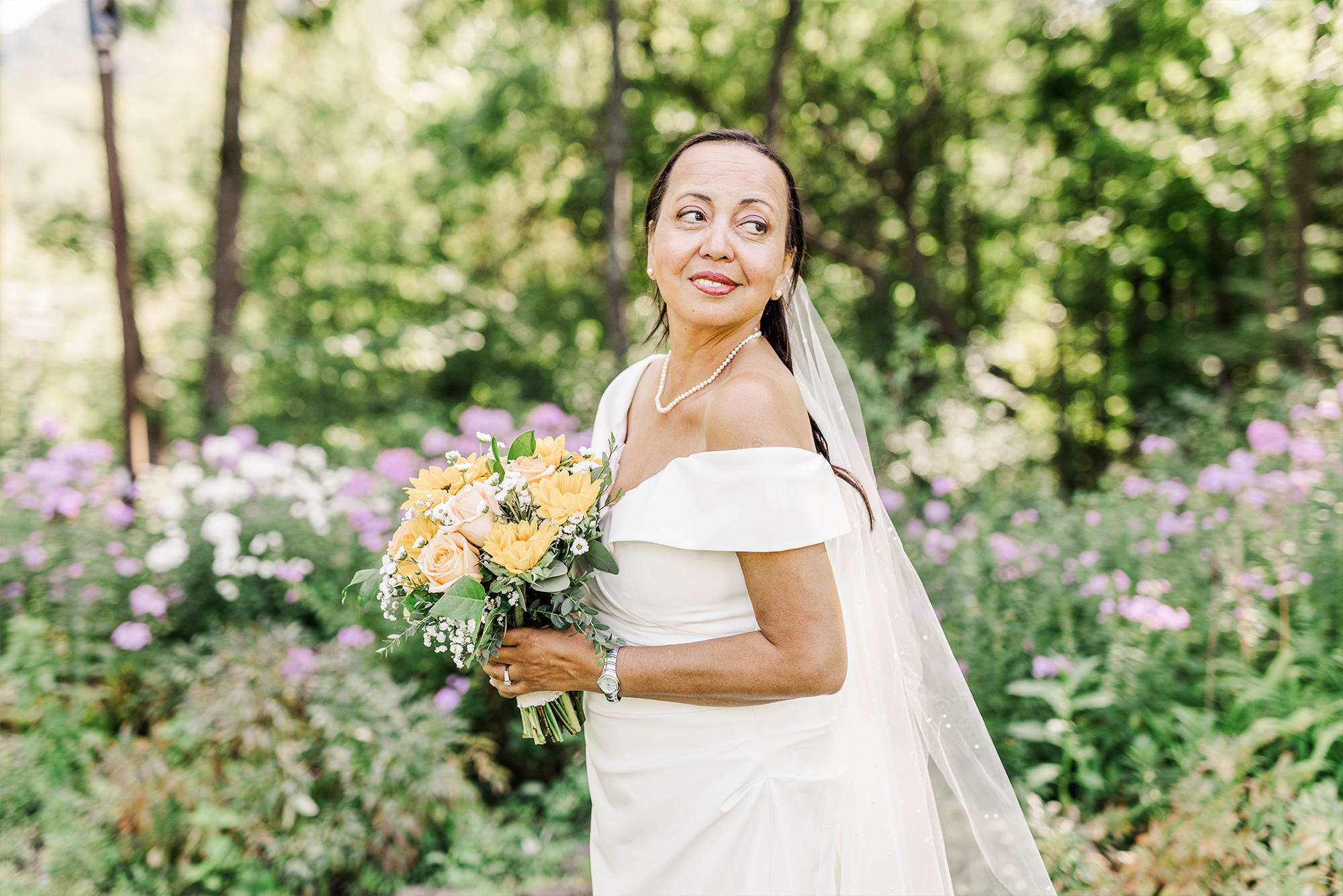 bride posing with bouquet in front of tall flowers and greenery
