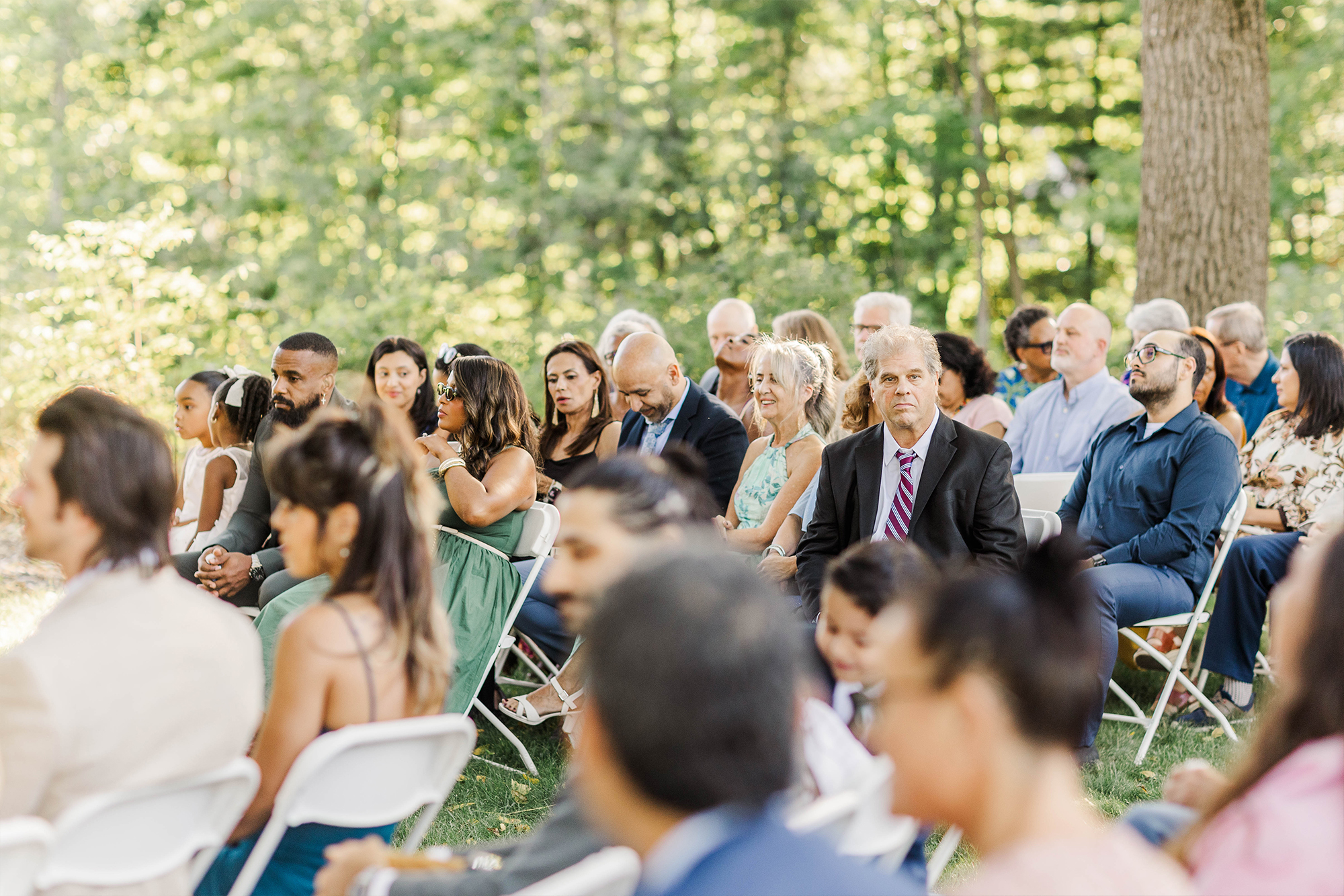 wedding guests sitting in foldable chairs surrounded by greenery