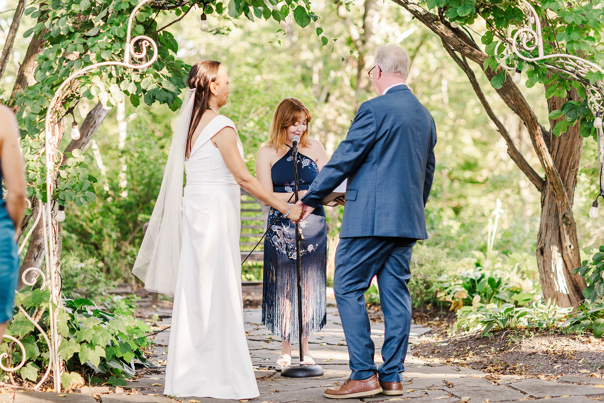 bride and groom underneath wedding arch with officiant at microphone stand