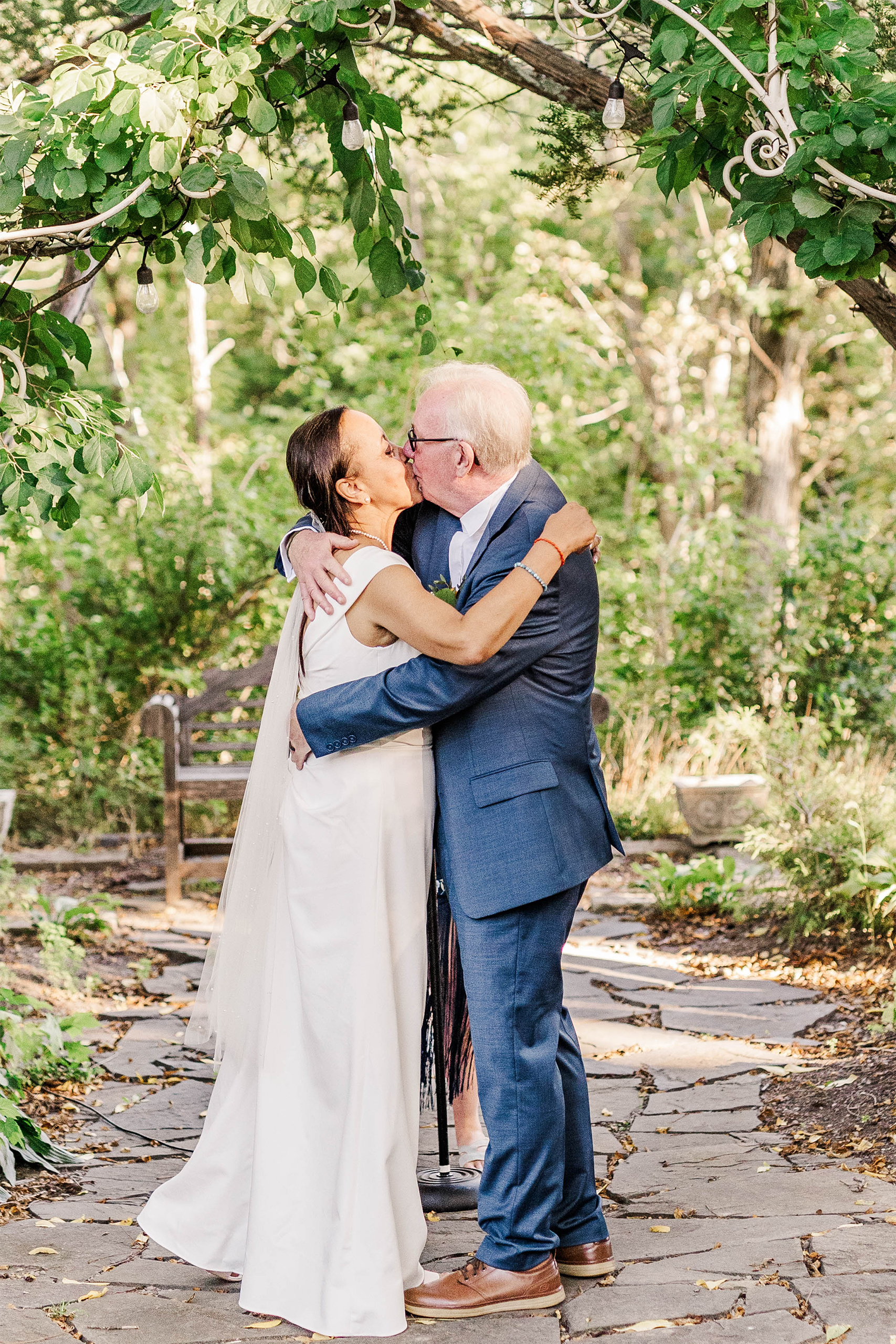 bride and groom sharing kiss underneath wedding arch with greenery