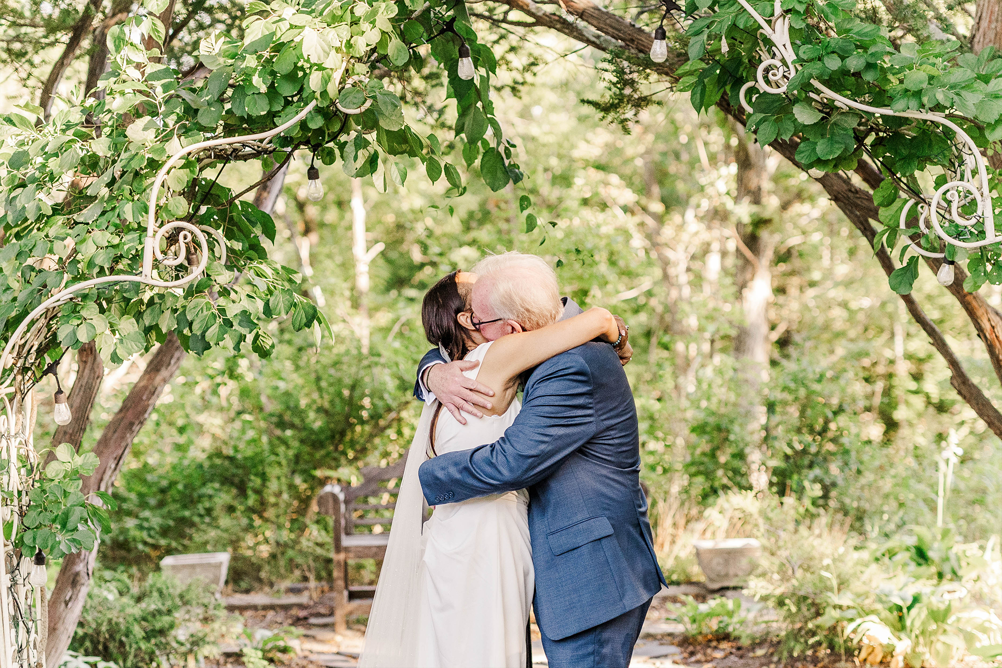 bride and groom sharing warm embrace underneath wedding arch with greenery